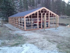 A wooden frame structure of a barn or shed under construction in an outdoor, rural field setting.