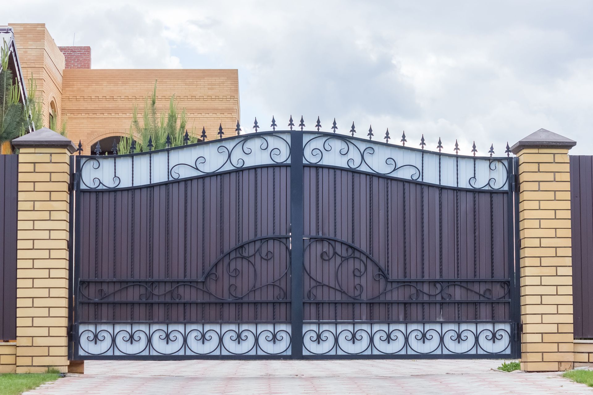 Brown metal driveway gate with decorative ironwork, set between brick pillars.