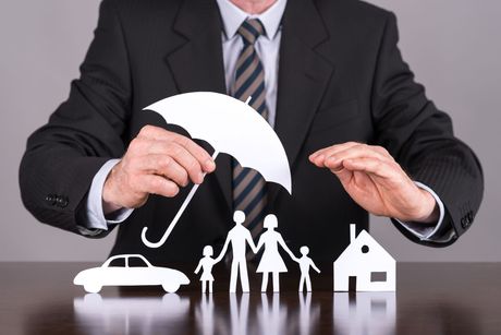 Person in suit holding paper umbrella over cut-out family, car, and house.
