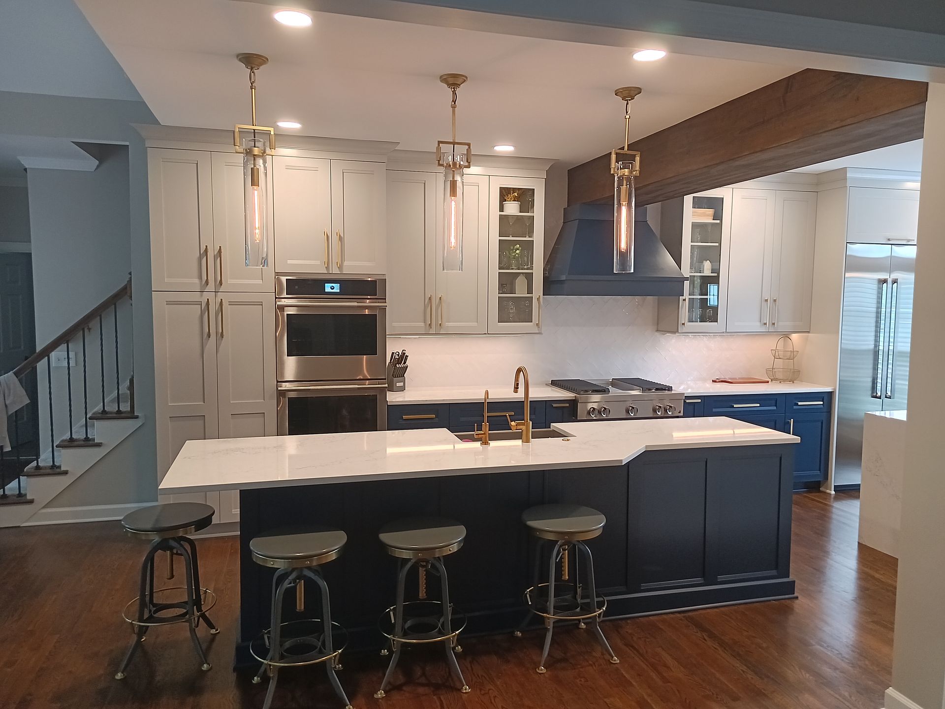 Modern kitchen with navy and white cabinets, island with stools, stainless steel appliances, and gold accents.