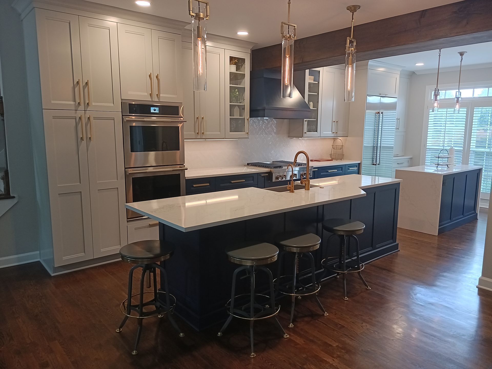 Modern kitchen with navy island, white countertops, wooden floors, and hanging lights.