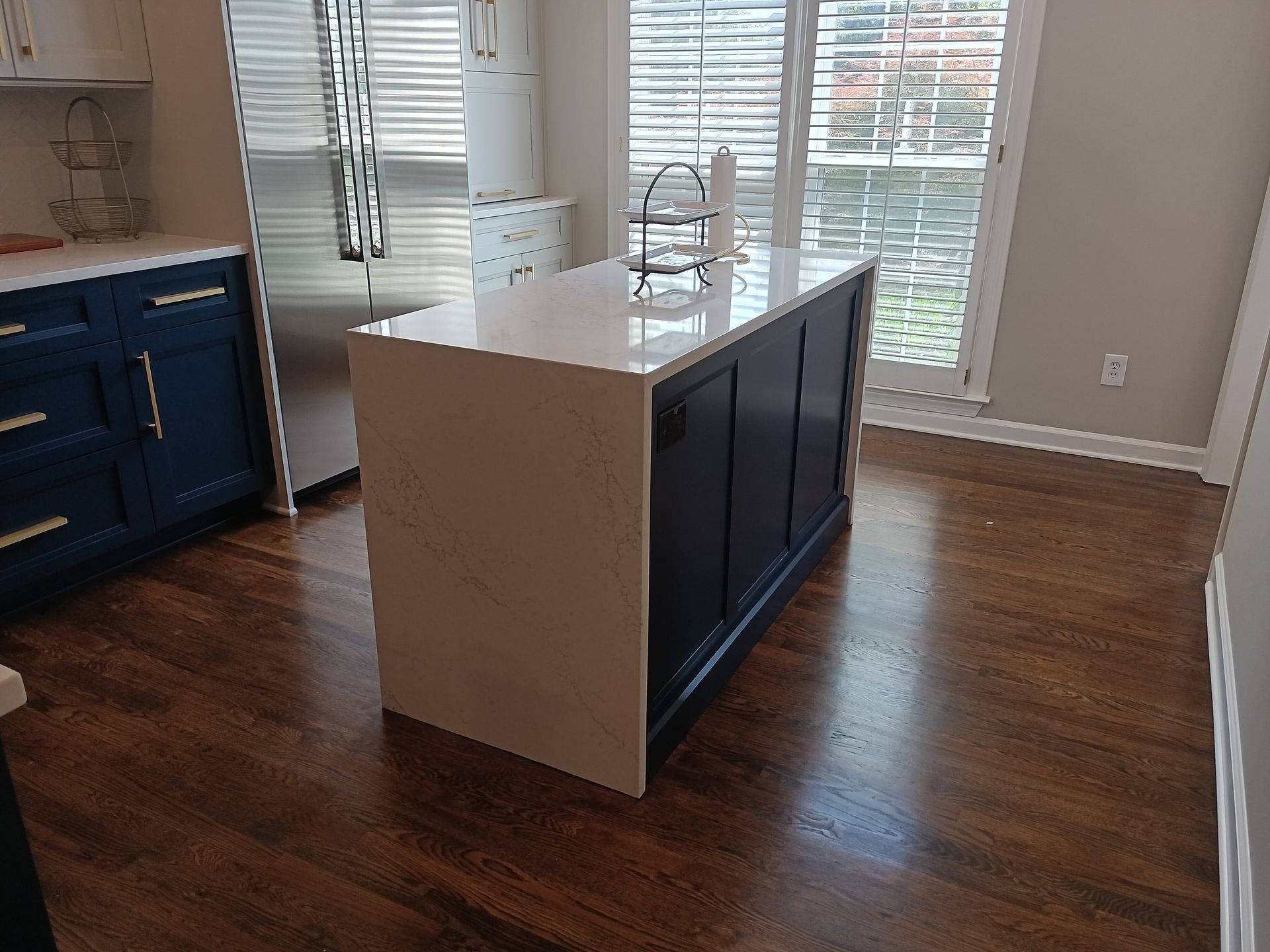 Kitchen with blue island, white countertop, stainless steel refrigerator, and dark wood floor.