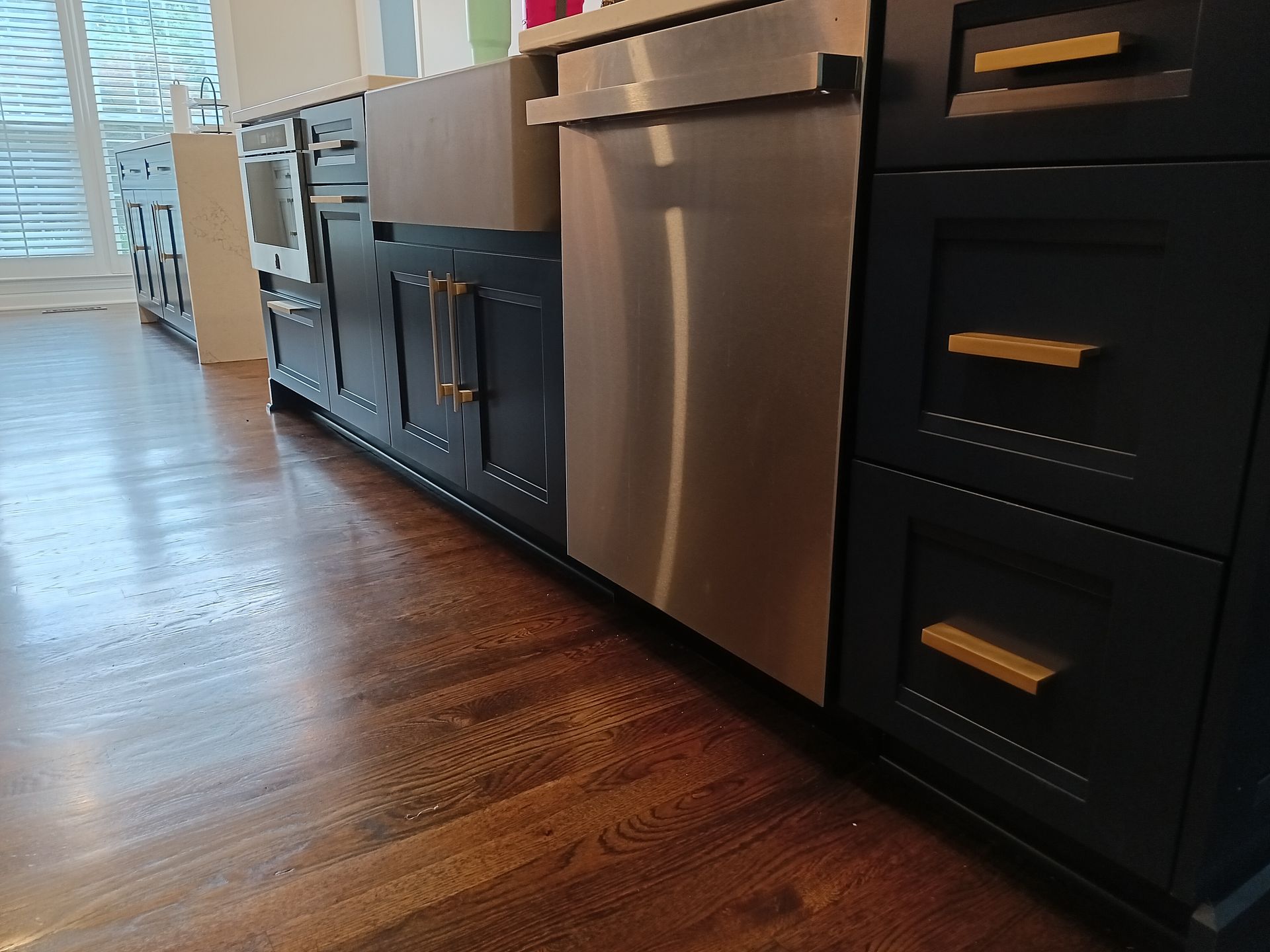 Dark kitchen cabinets with gold hardware and stainless steel appliances against wood floors.