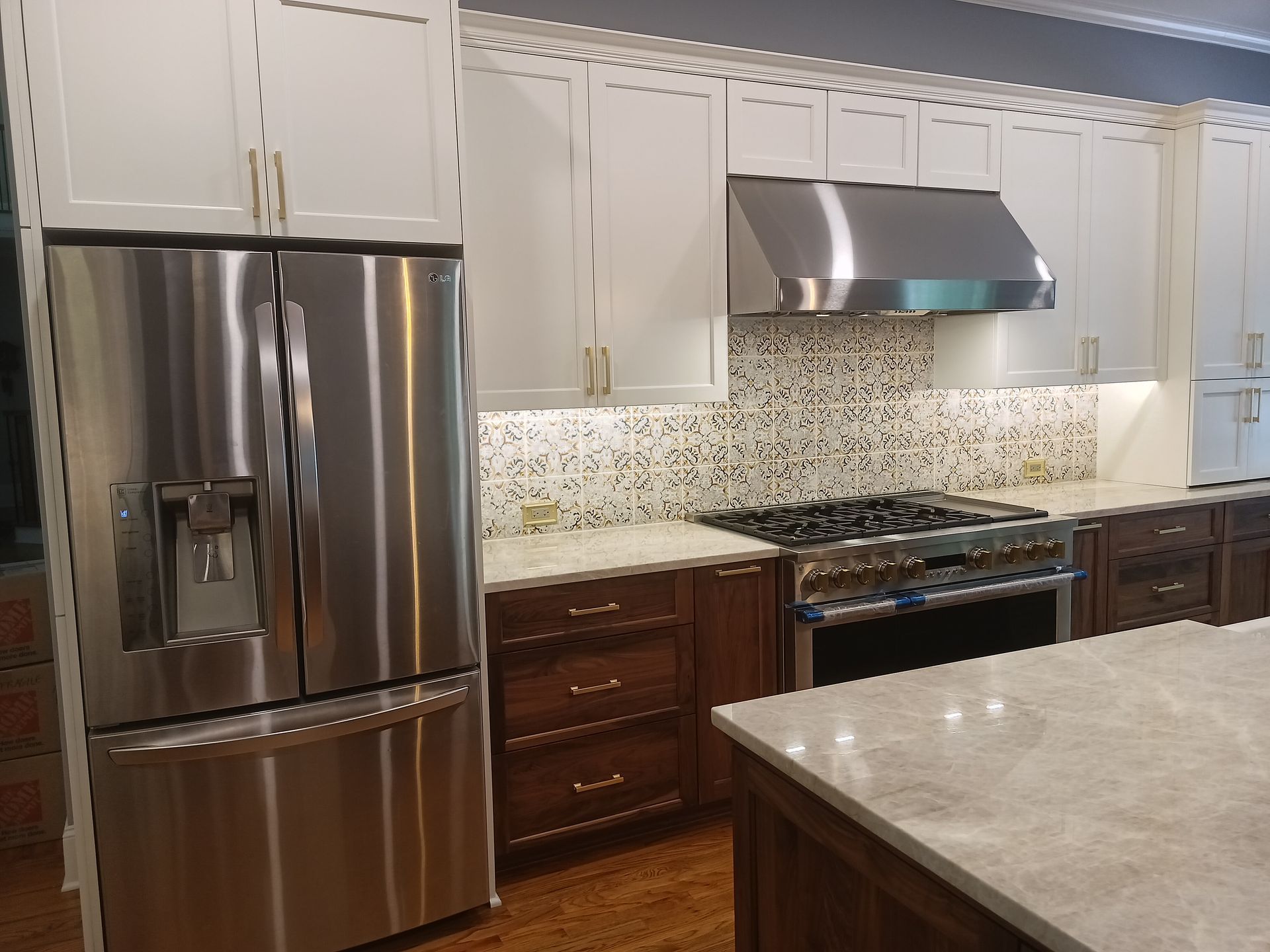 Modern kitchen with white upper cabinets, stainless steel appliances, and a brown base with marble countertops.