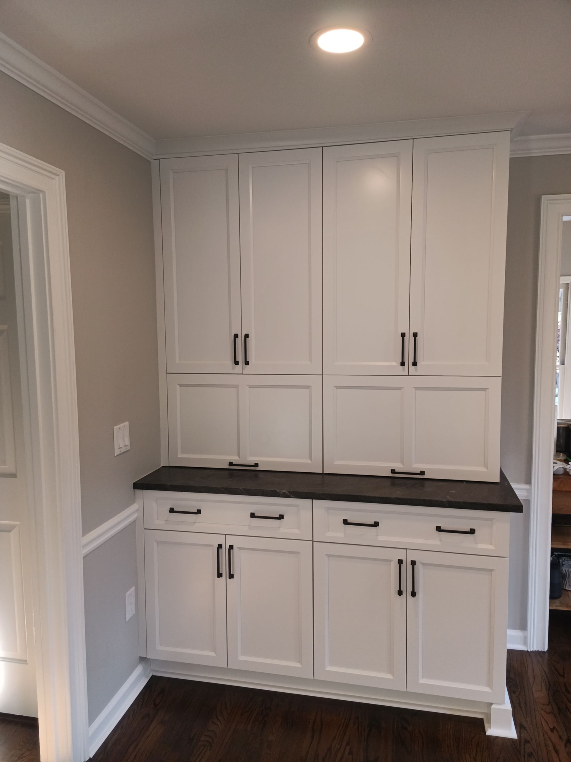 White pantry cabinets with dark countertops and black hardware in a corner setting.