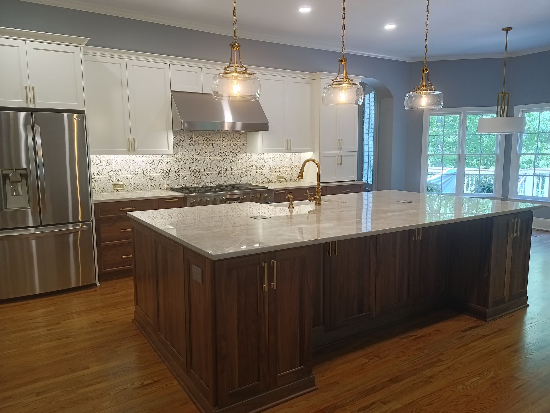 Modern kitchen with brown island, white upper cabinets, stainless steel appliances, and gold pendant lights.