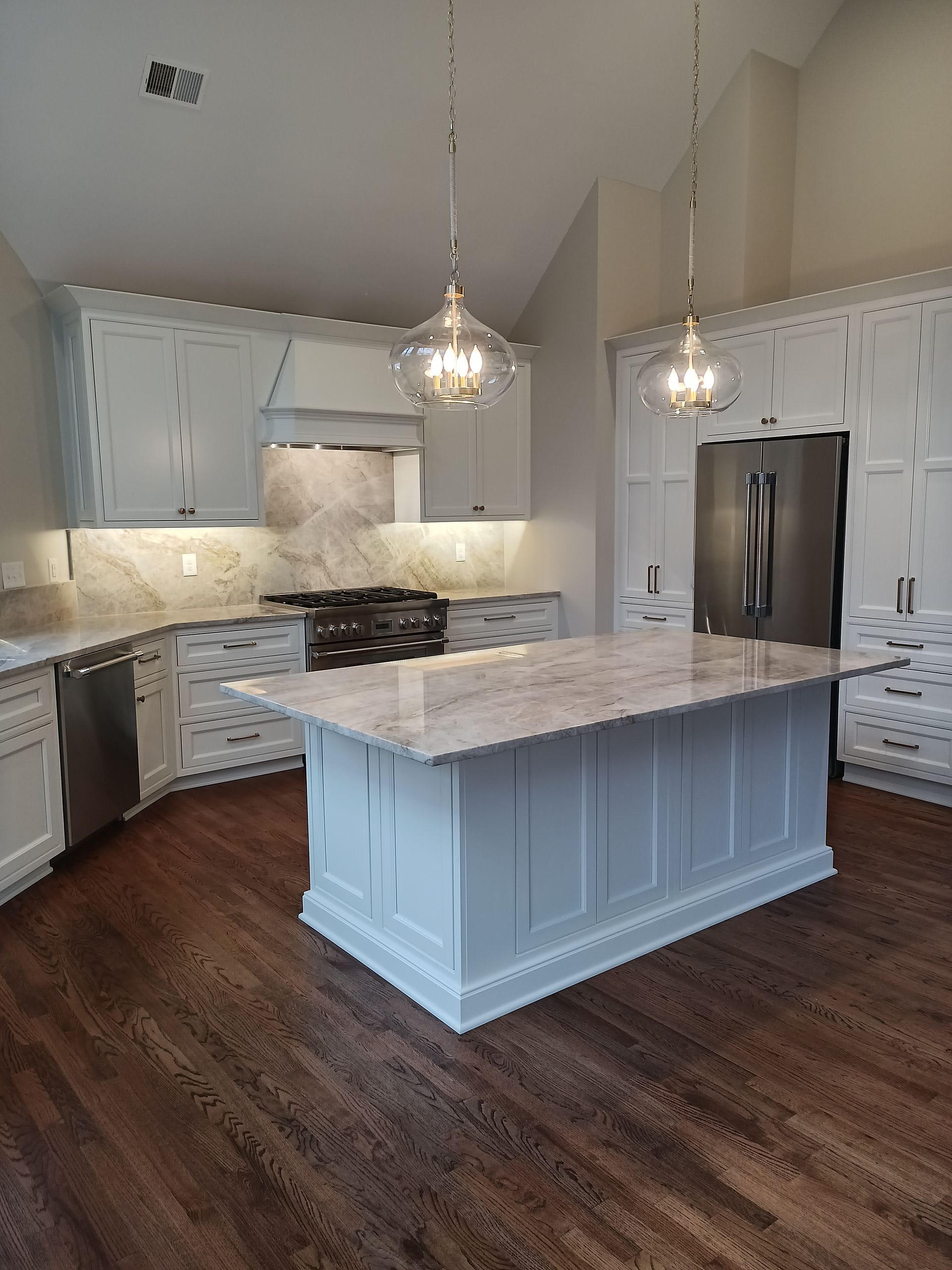 Kitchen with white cabinets, marble countertops, and a blue island with pendant lights.