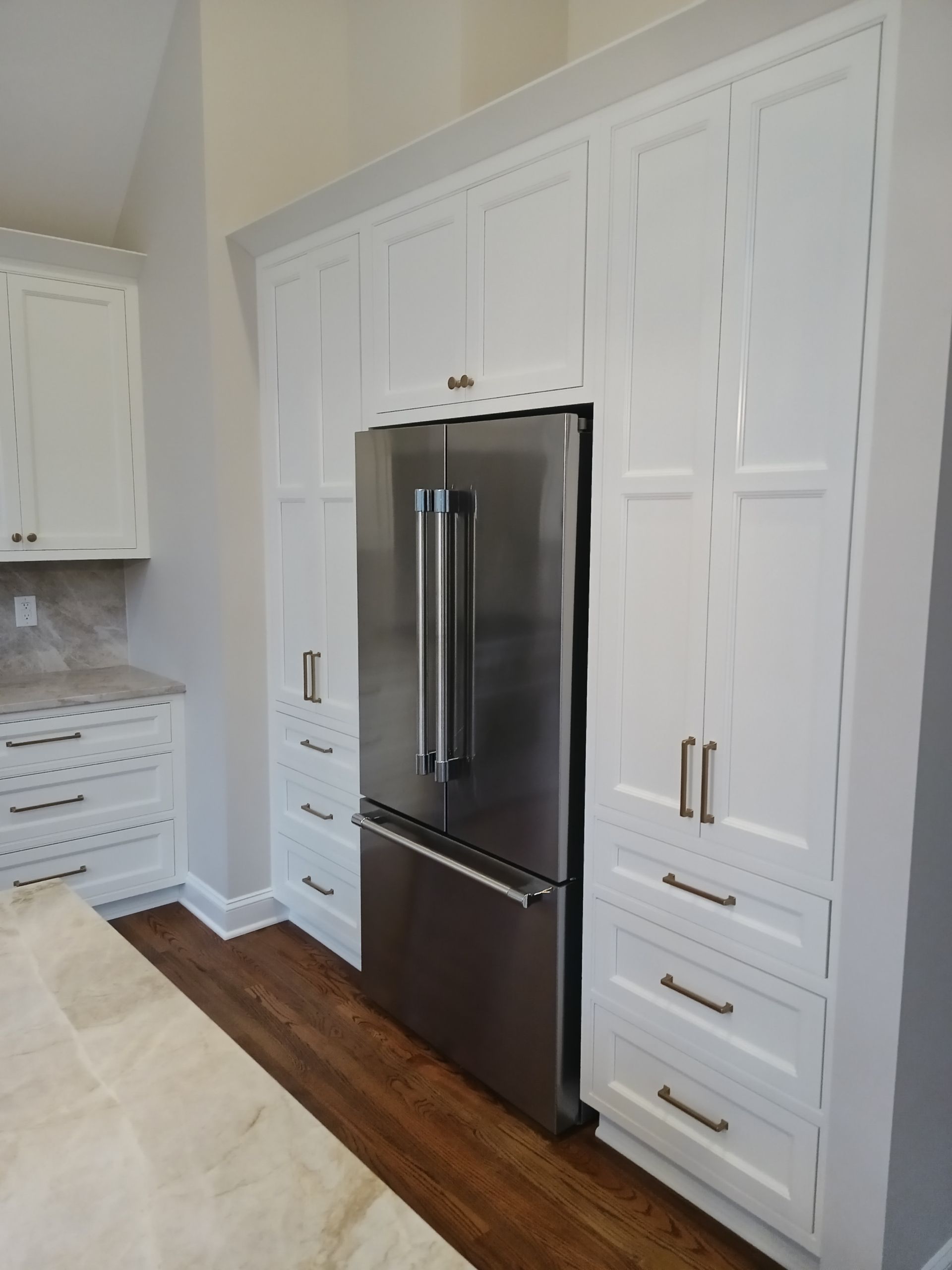 Stainless steel refrigerator built into white cabinets in a kitchen with wooden floor.