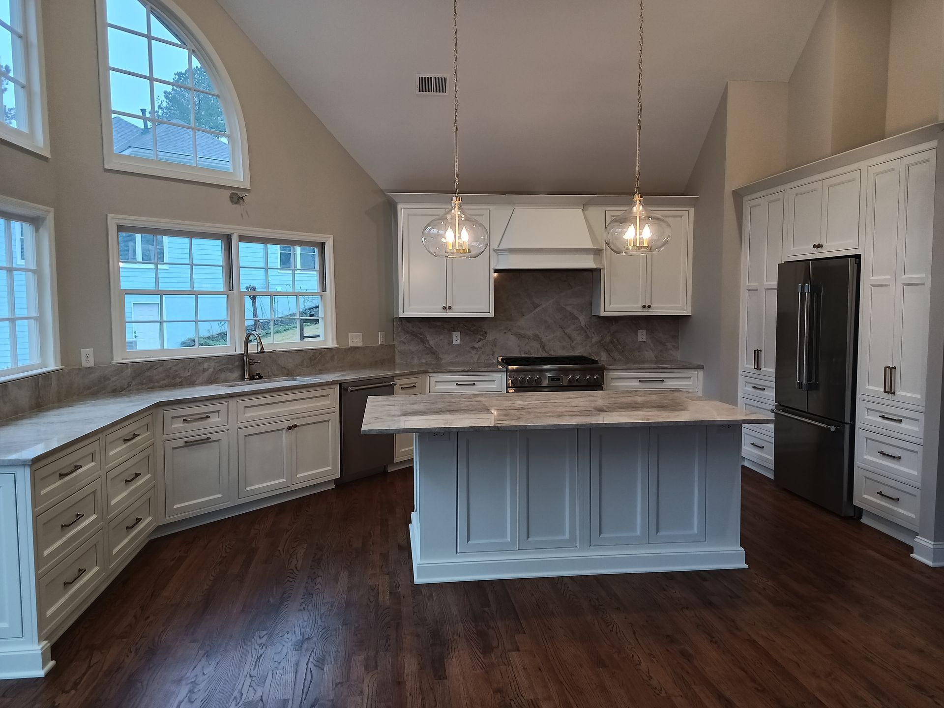 Modern kitchen with white cabinets, gray island, stainless steel appliances, and wood flooring.