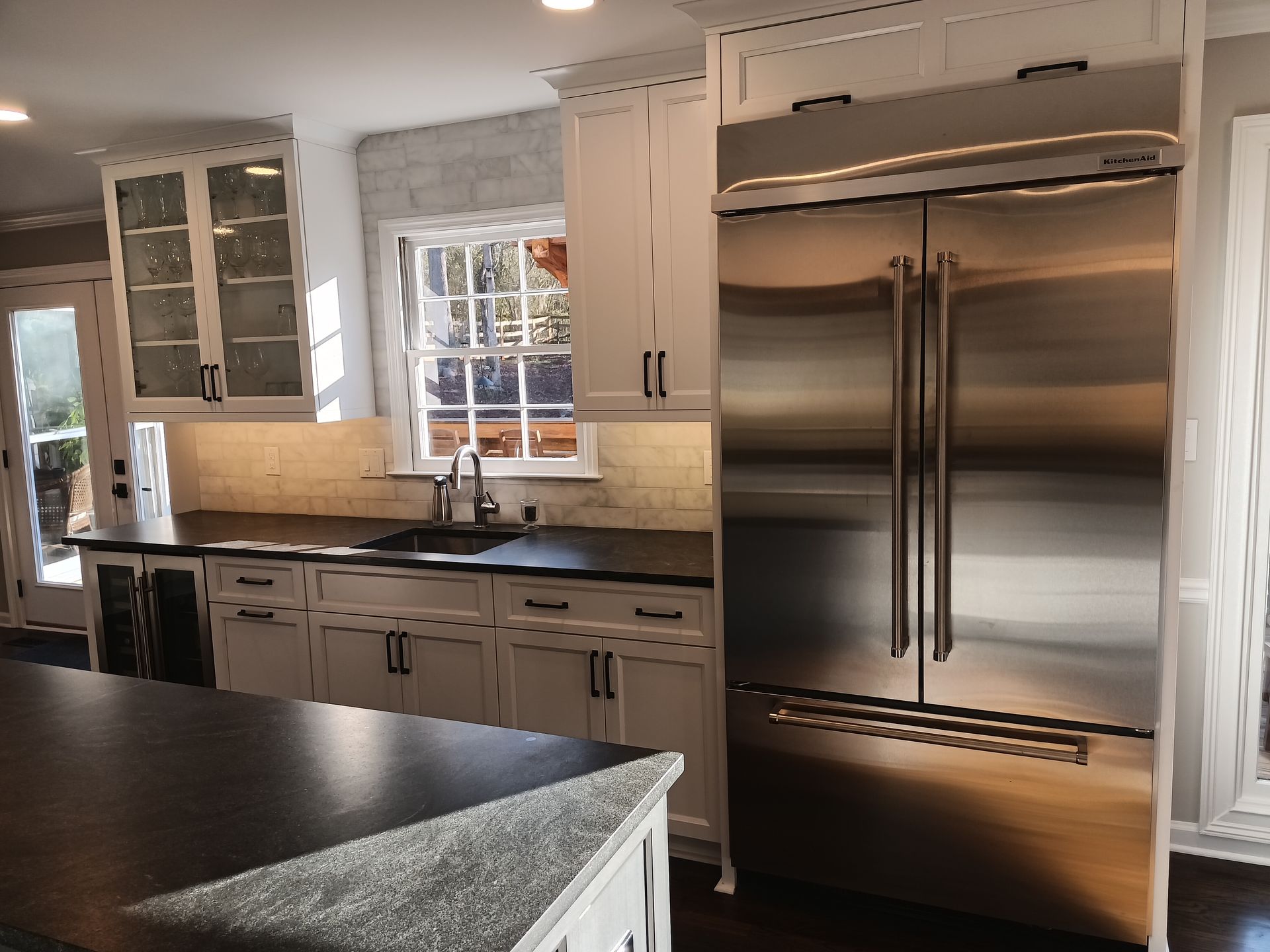 Stainless steel refrigerator in a bright kitchen with white cabinets and a dark countertop.