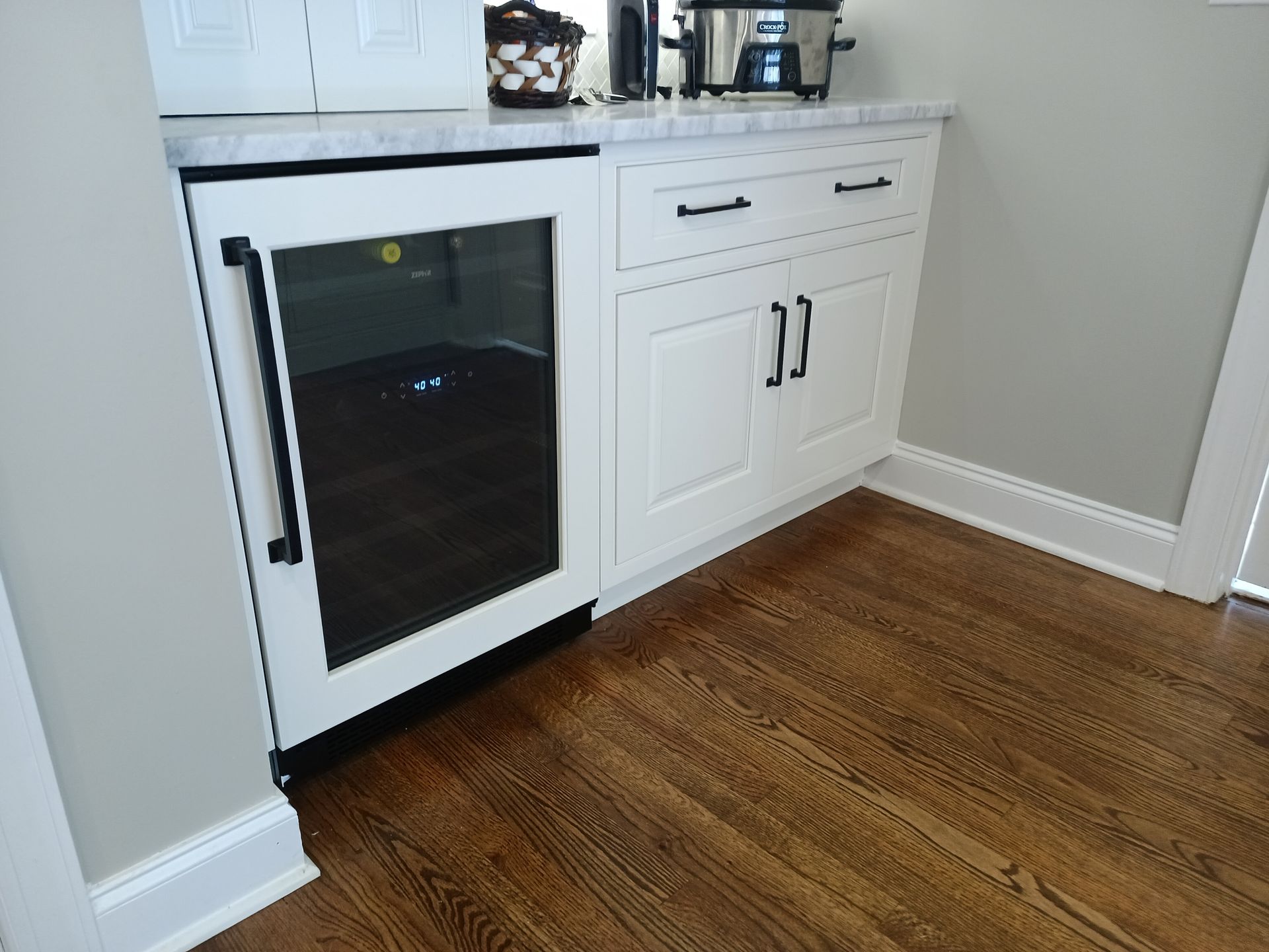 Built-in white cabinet with a wine fridge, marble countertop, and dark wood floor.
