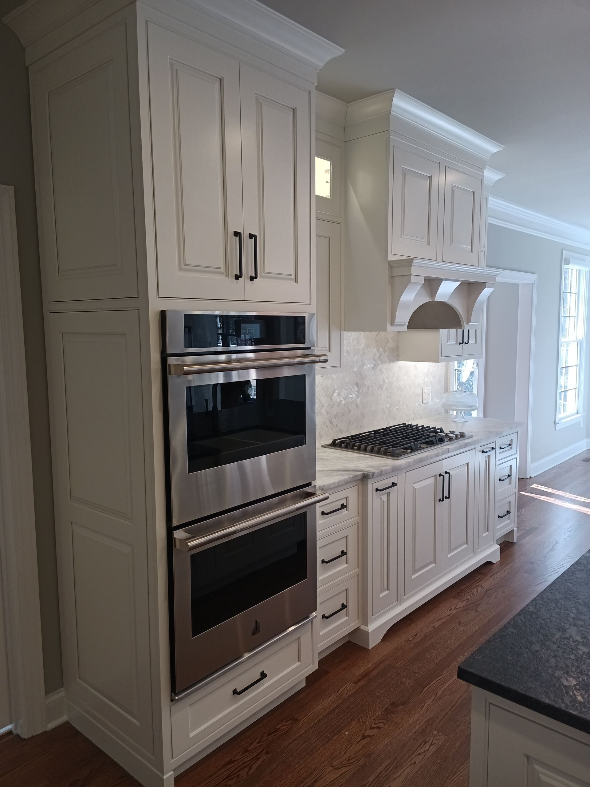 White kitchen with stainless steel oven and cabinets, hardwood floor, and marble countertop.