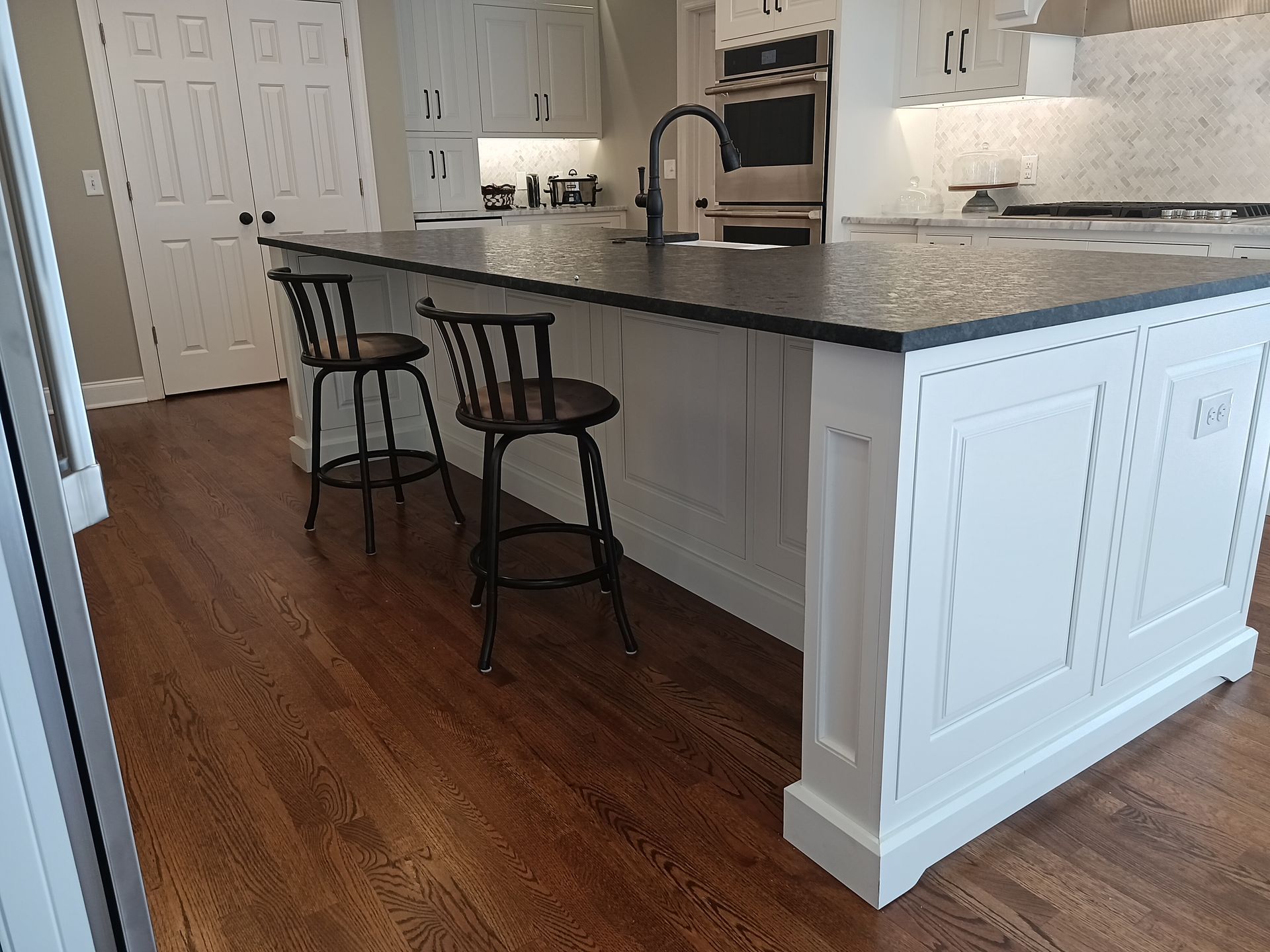 A kitchen island with black countertop and white cabinets. Two black stools on a wood floor.