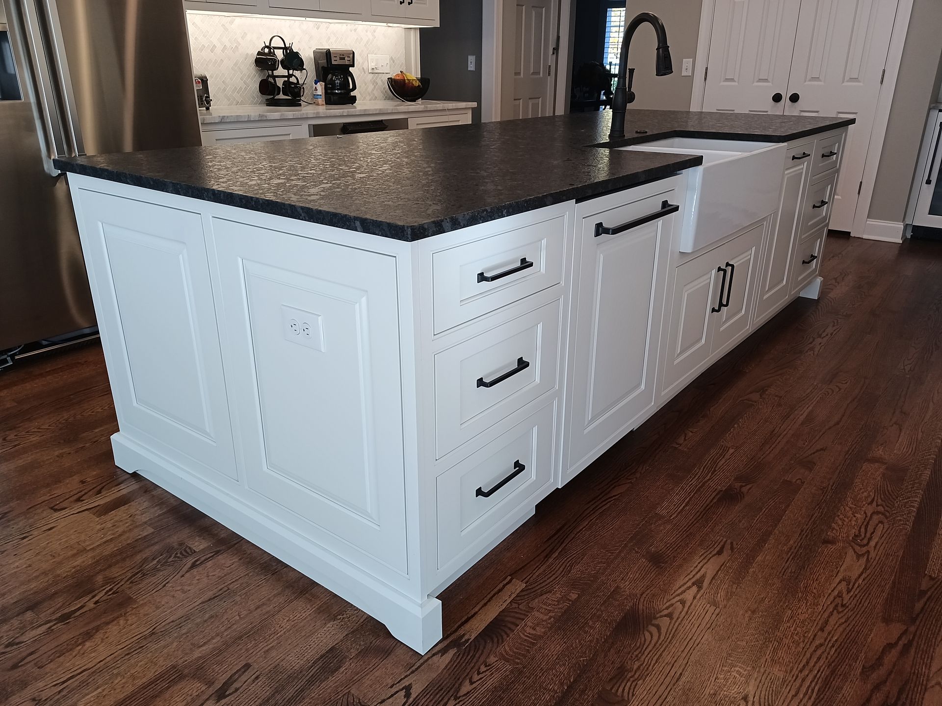 White kitchen island with black countertop and hardware on a wooden floor.