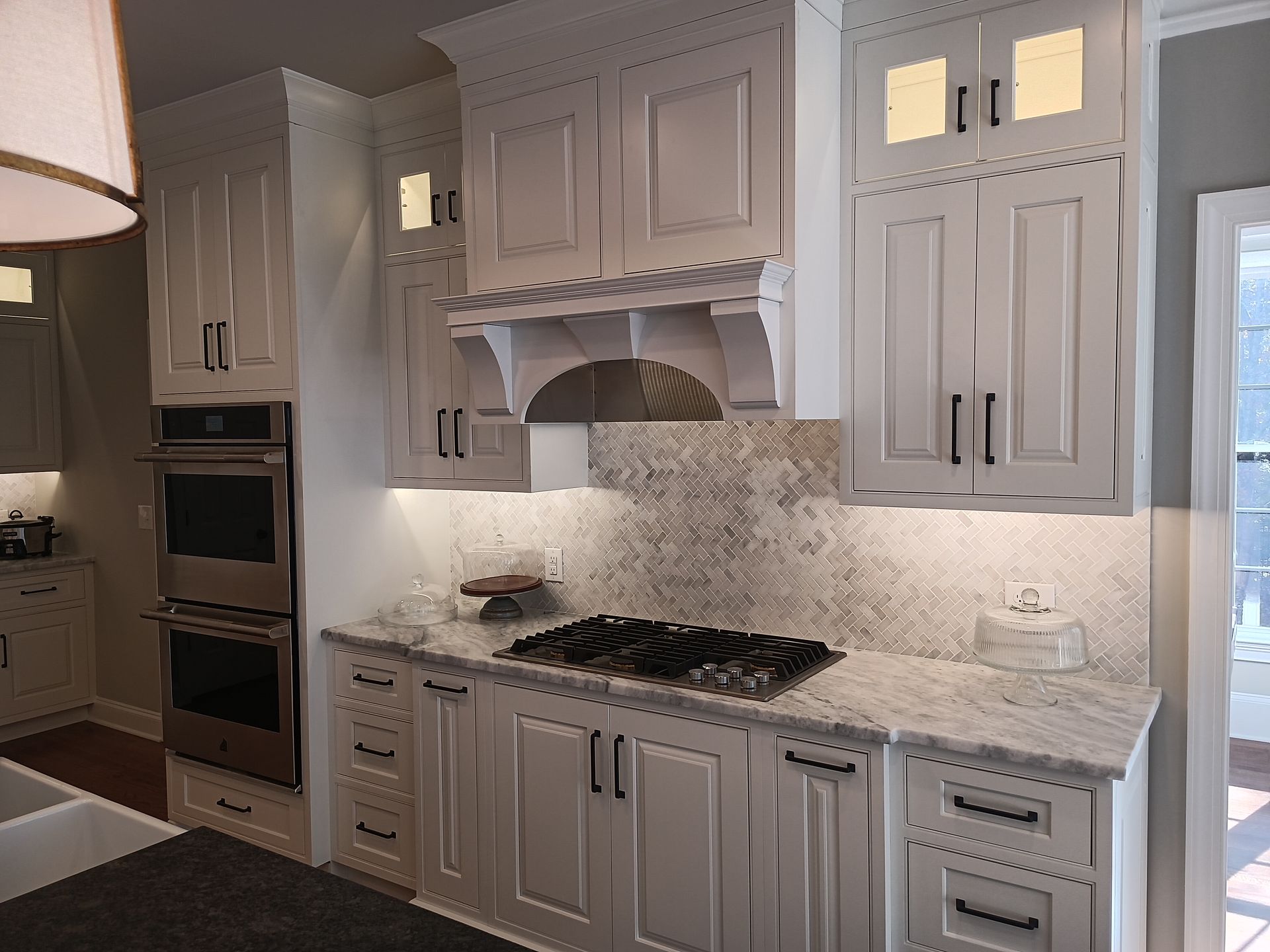 White kitchen with cabinetry, stove, and stone backsplash; overhead lighting.