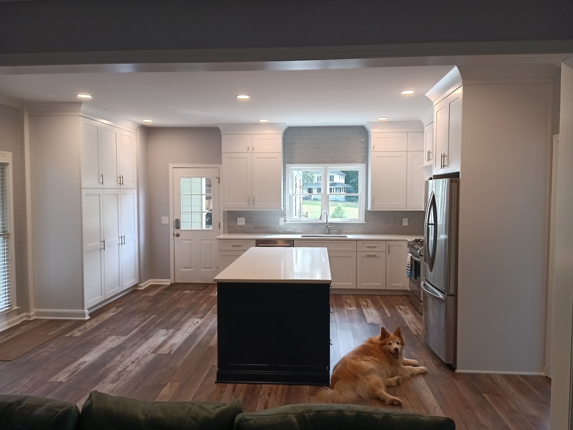 Bright kitchen with white cabinets, dark island, dog lying on wood floor.