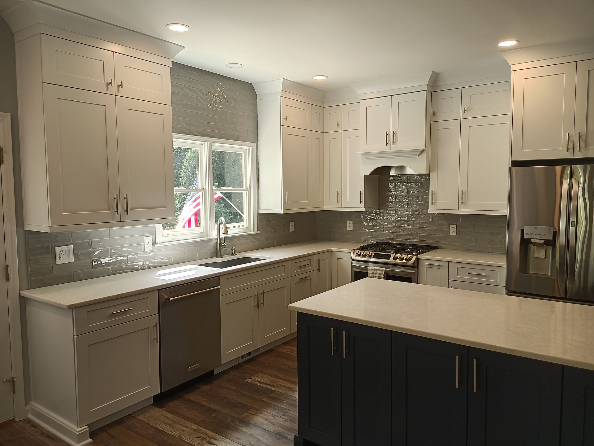 Modern kitchen with white cabinets, blue island, stainless steel appliances, and hardwood floors.