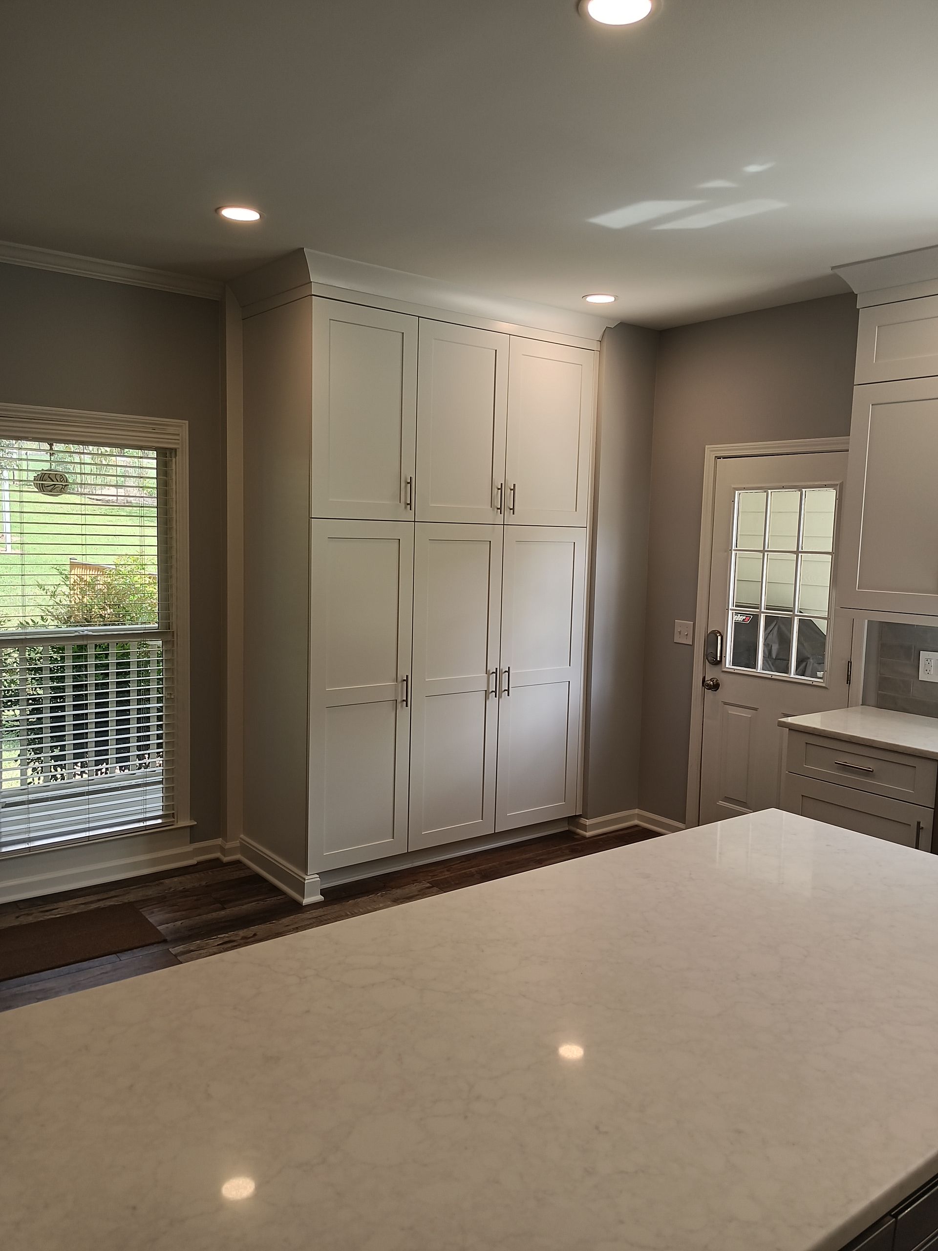 Kitchen with white cabinets, a light-colored countertop, and a door and window on the left side.