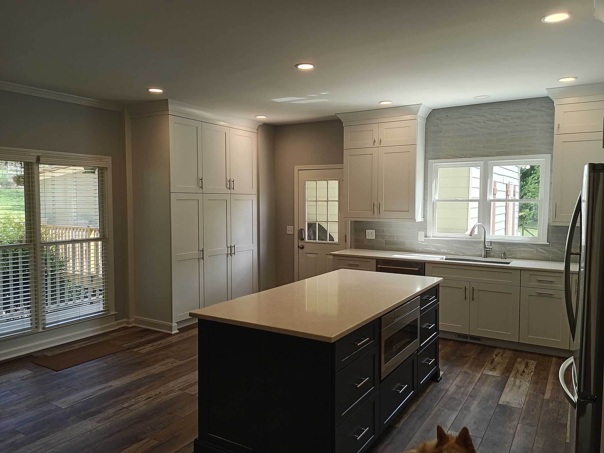 Modern kitchen with island, white cabinets, and dark wood floors; a dog is in the foreground.