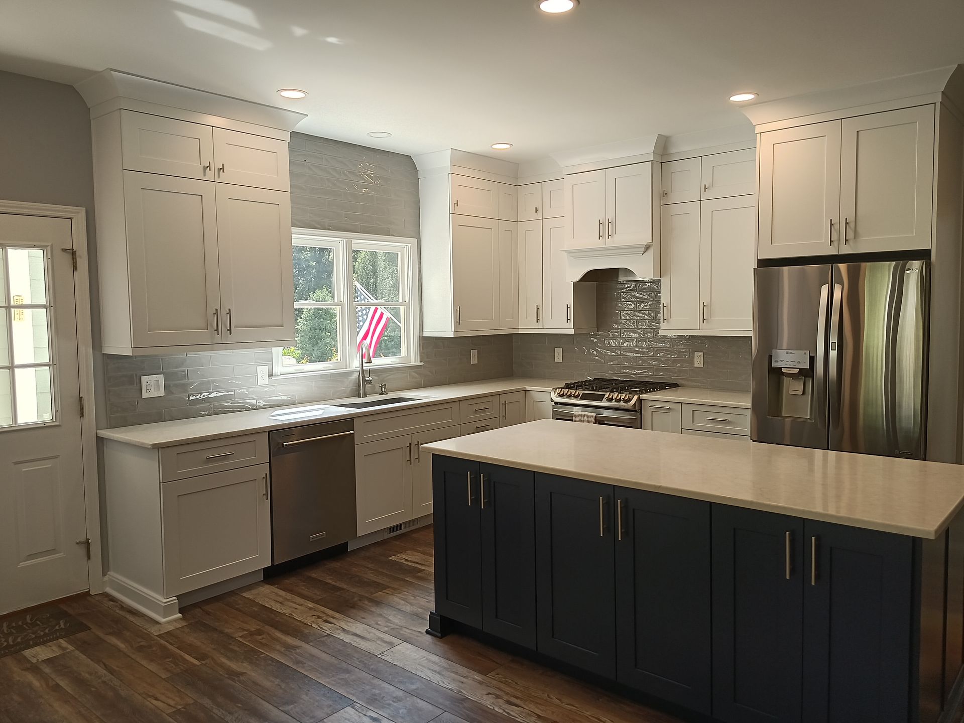 A modern kitchen with white cabinets, dark blue island, stainless steel appliances, and wooden floors.