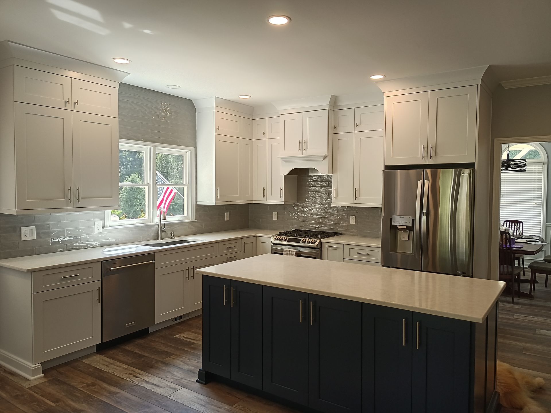 Modern kitchen with white cabinets, navy island, stainless steel appliances, and wood floors.