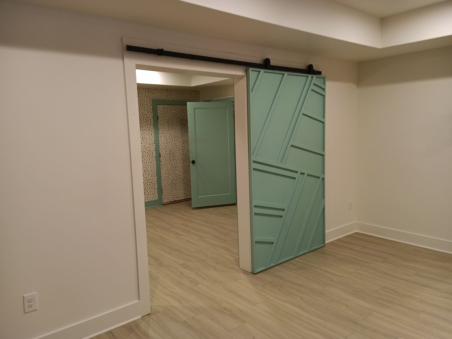 Room with a sliding turquoise barn door, another door and a mosaic wall in the background.