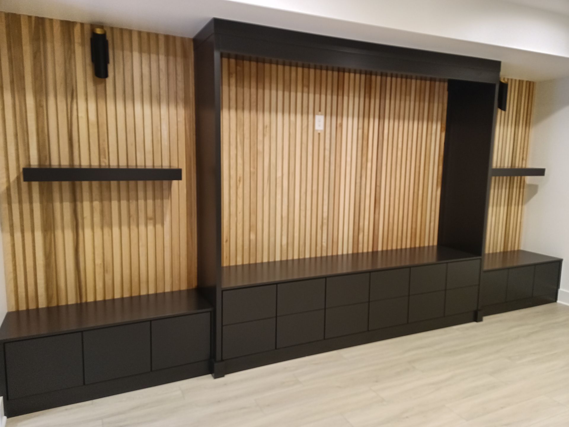 Built-in entertainment center with black cabinets, wooden slat wall, and floating shelves.