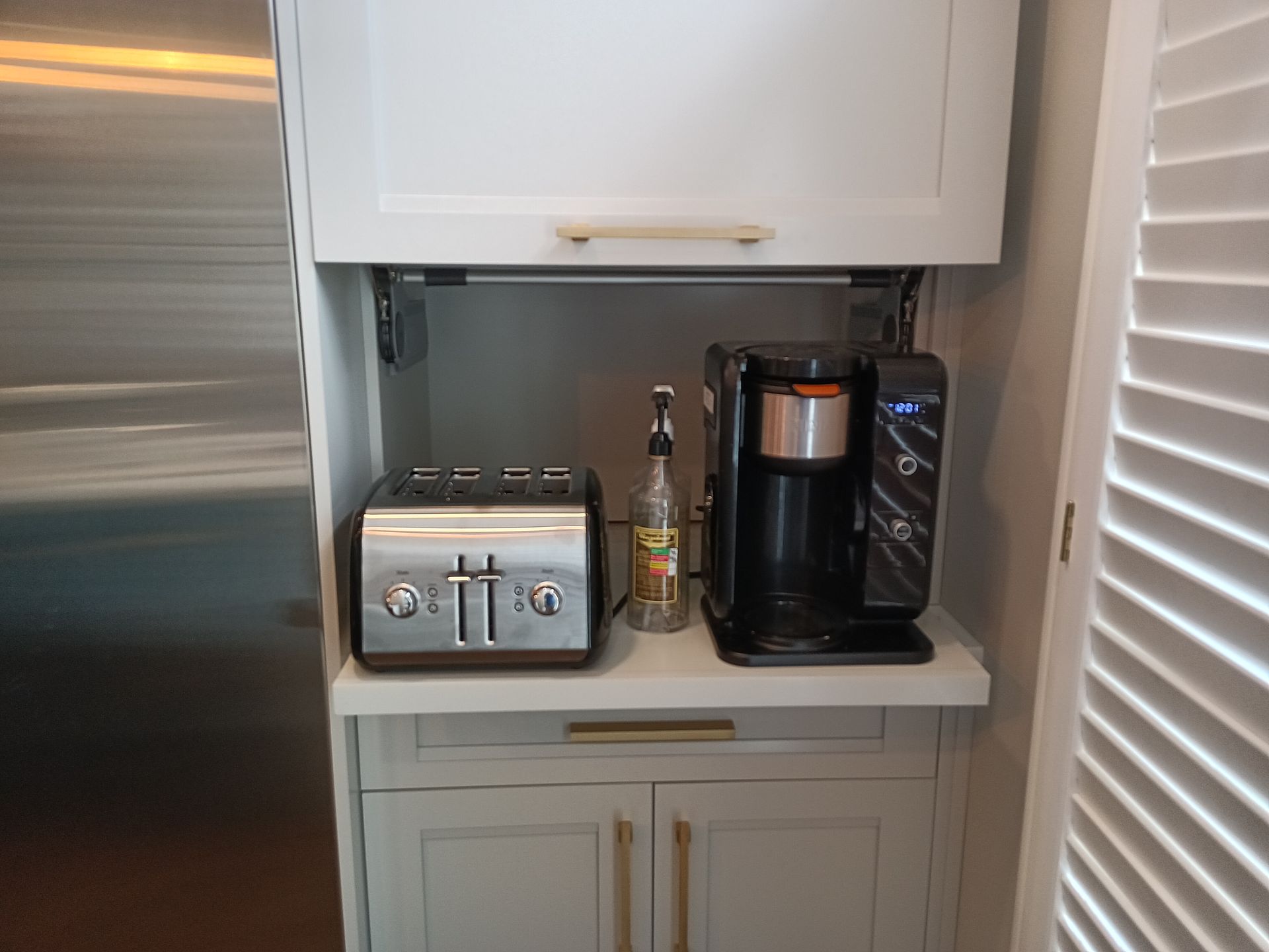Built-in kitchen coffee station with toaster, syrup, and coffee maker, next to fridge.