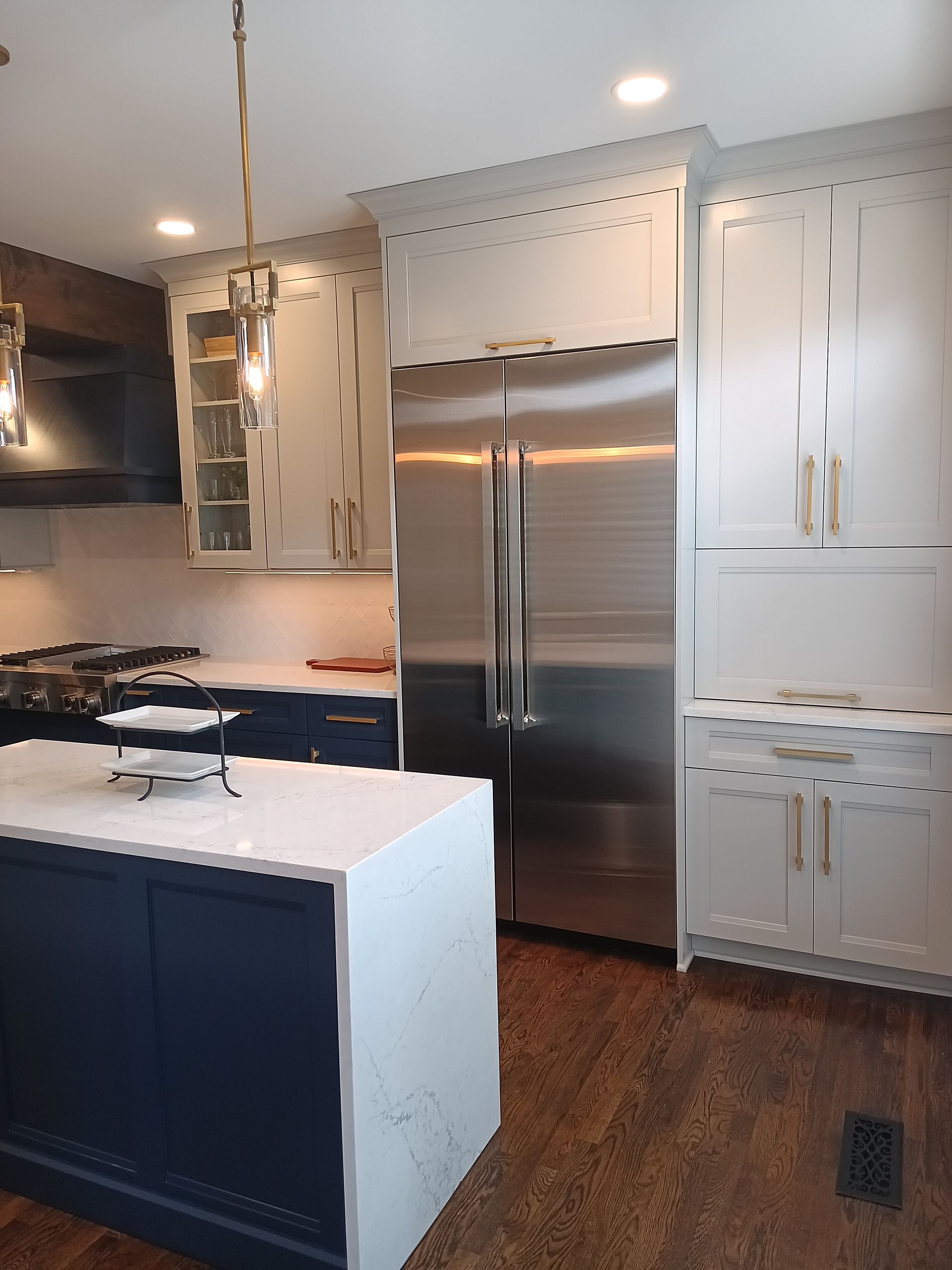 Kitchen with stainless steel refrigerator, white and navy cabinets, and gold hardware.
