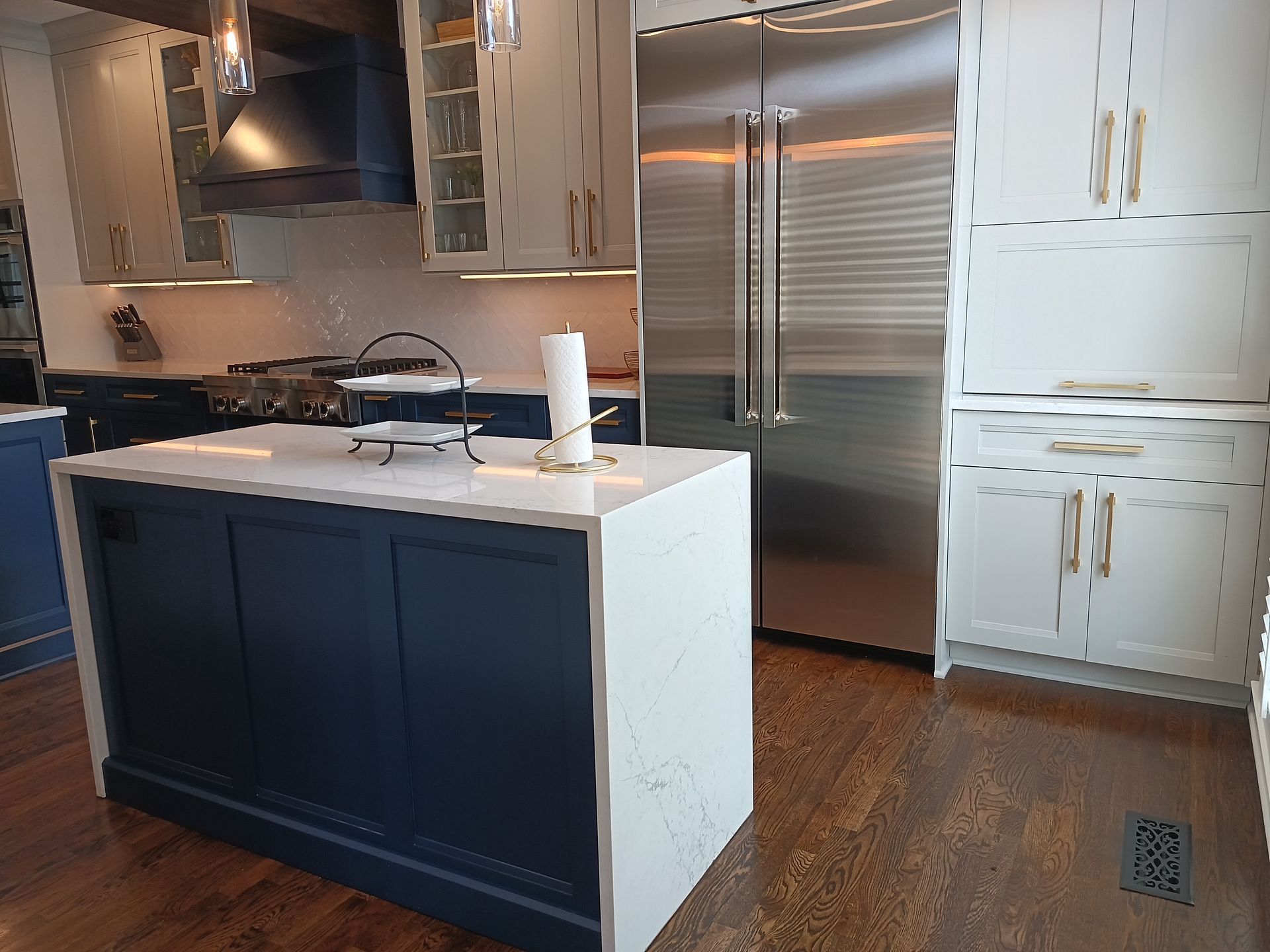 Modern kitchen with a blue island, stainless steel fridge, and white and blue cabinets.
