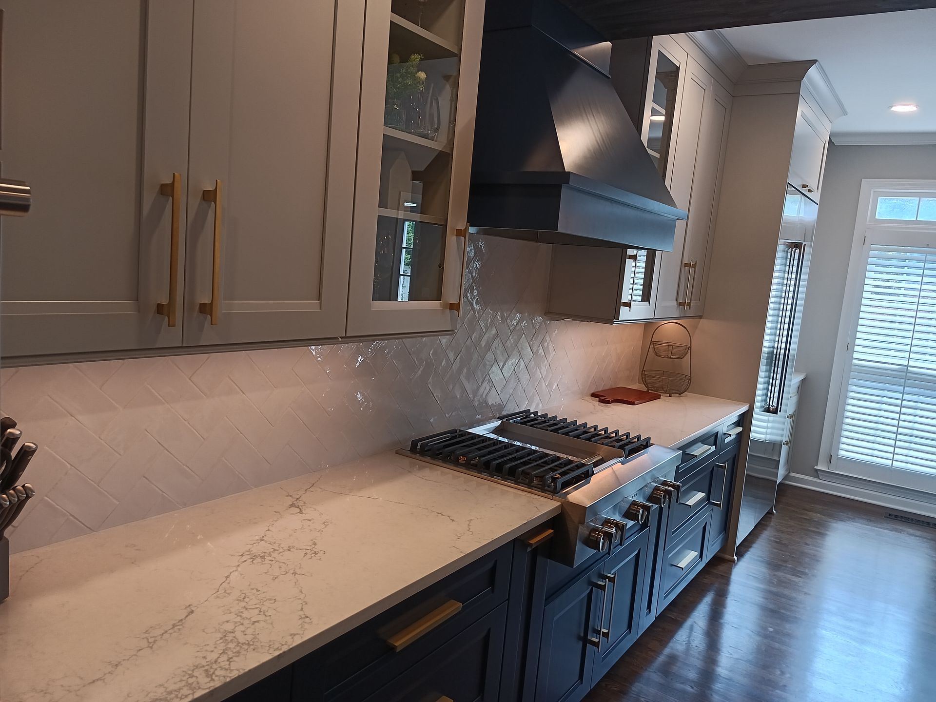 Modern kitchen with gray cabinets, gold hardware, white countertops, and a dark range hood.