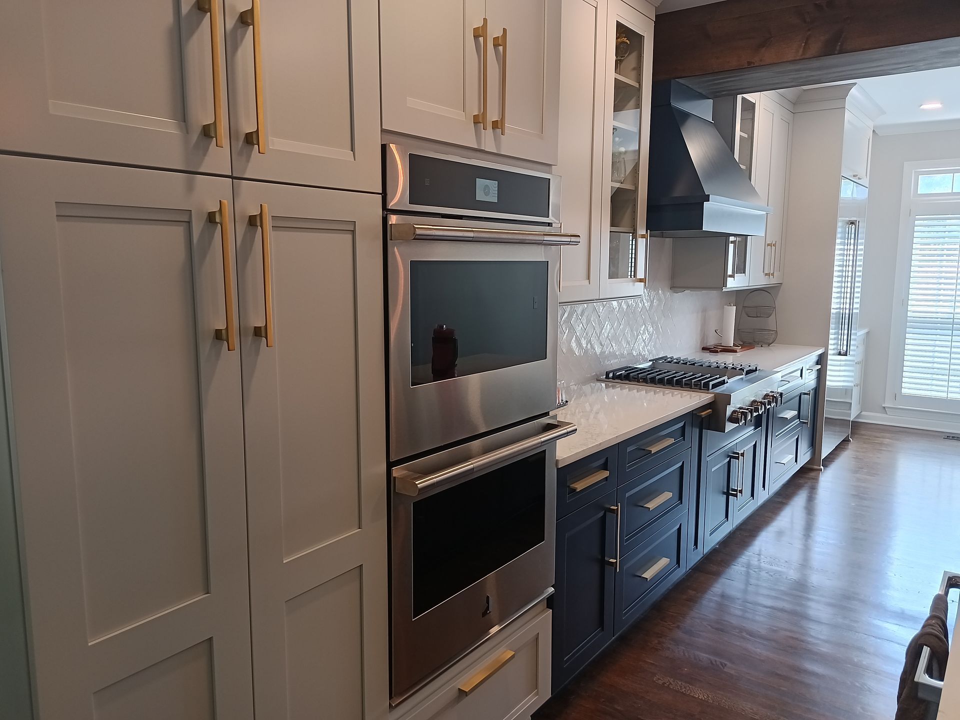 Modern kitchen with white and navy cabinets, stainless steel oven, and gold hardware.