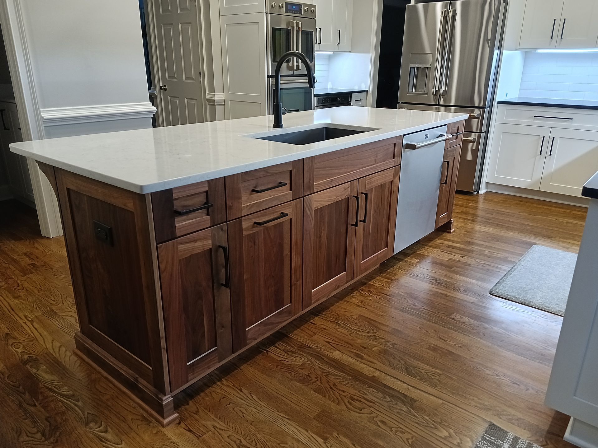 Kitchen island with dark wood cabinets, white countertop, and built-in dishwasher, on a wood floor.