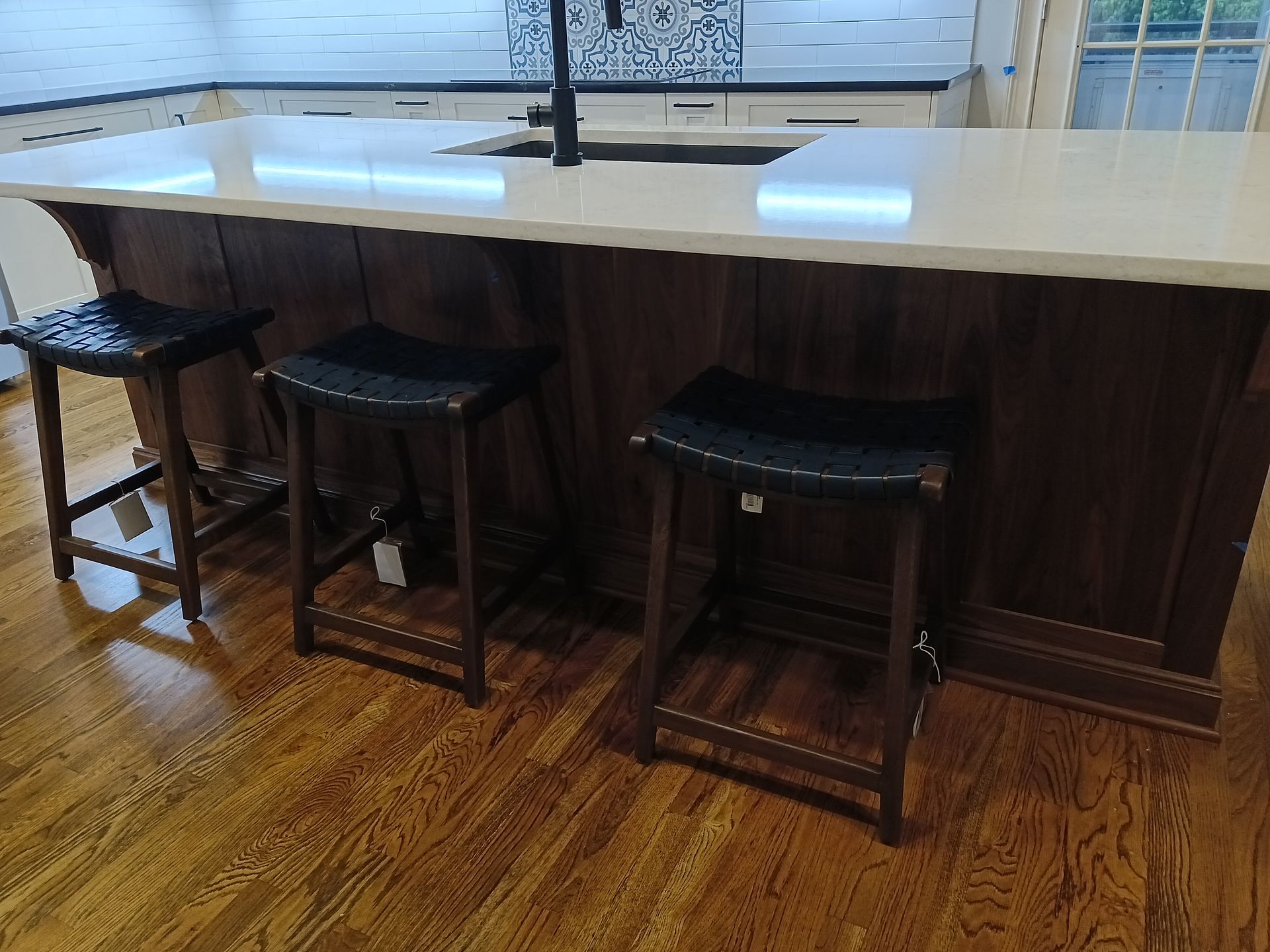 Three leather bar stools at a kitchen island with a white countertop and dark wooden cabinetry.