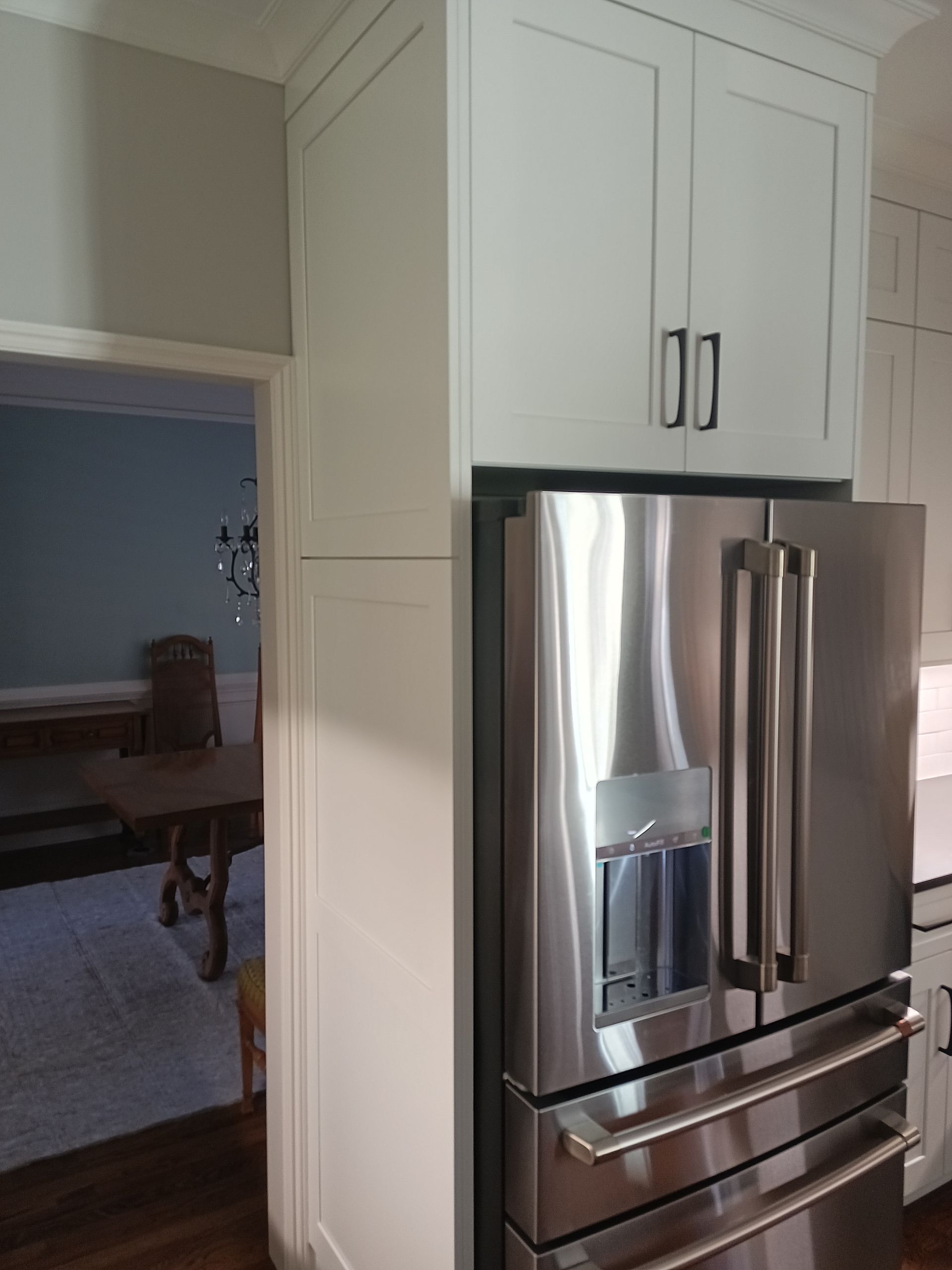 Stainless steel refrigerator next to white cabinets. An archway into a room on the left.