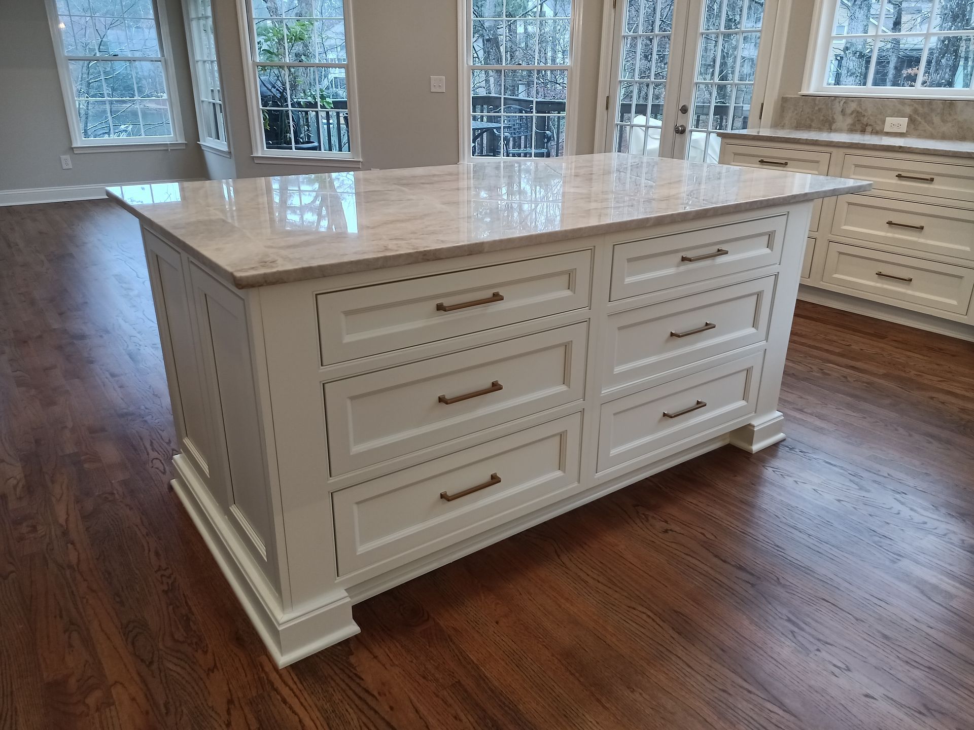 White kitchen island with marble countertop and drawers on wood floor.