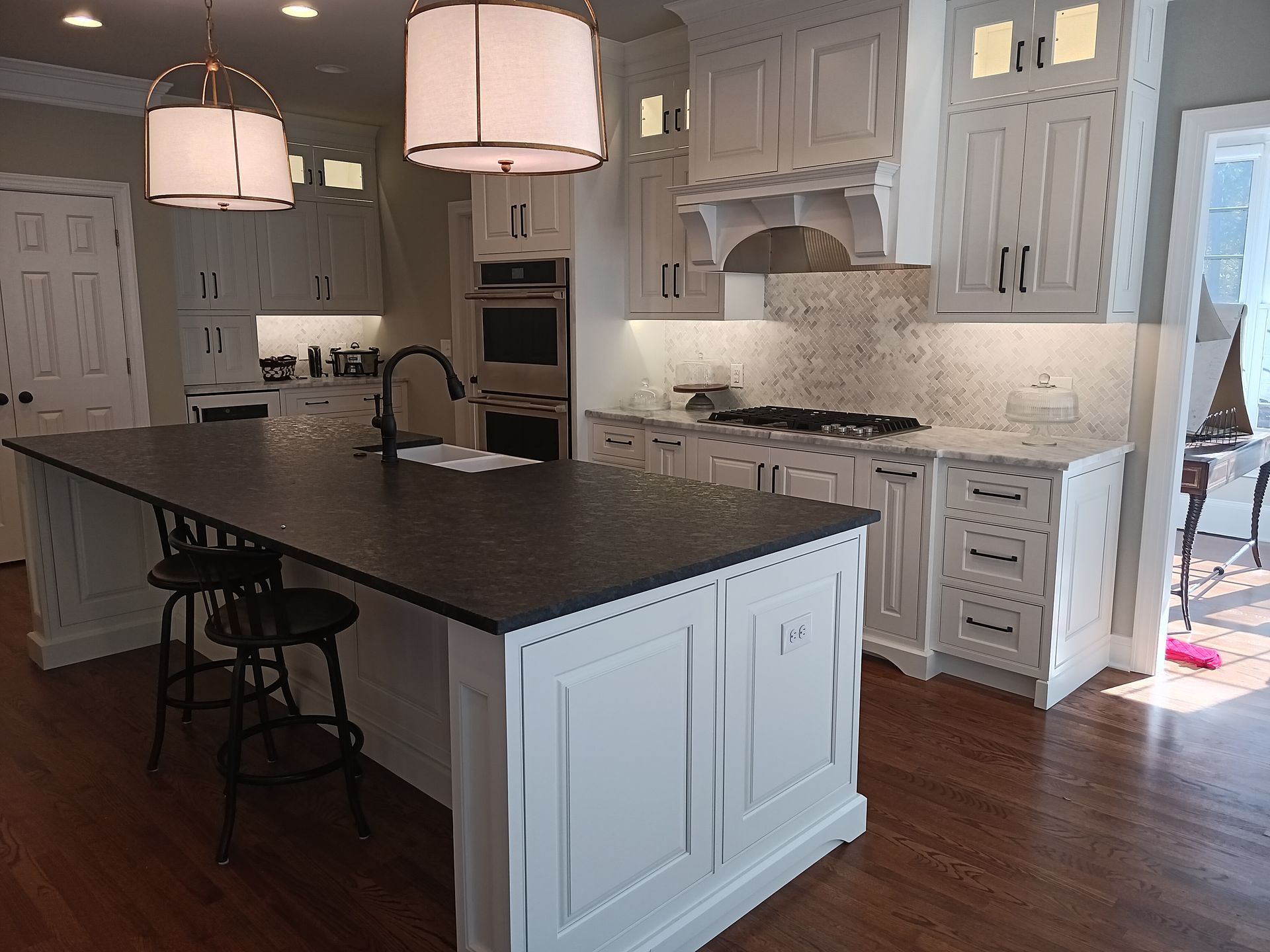 White kitchen with a black island countertop, pendant lights, and stainless steel appliances.