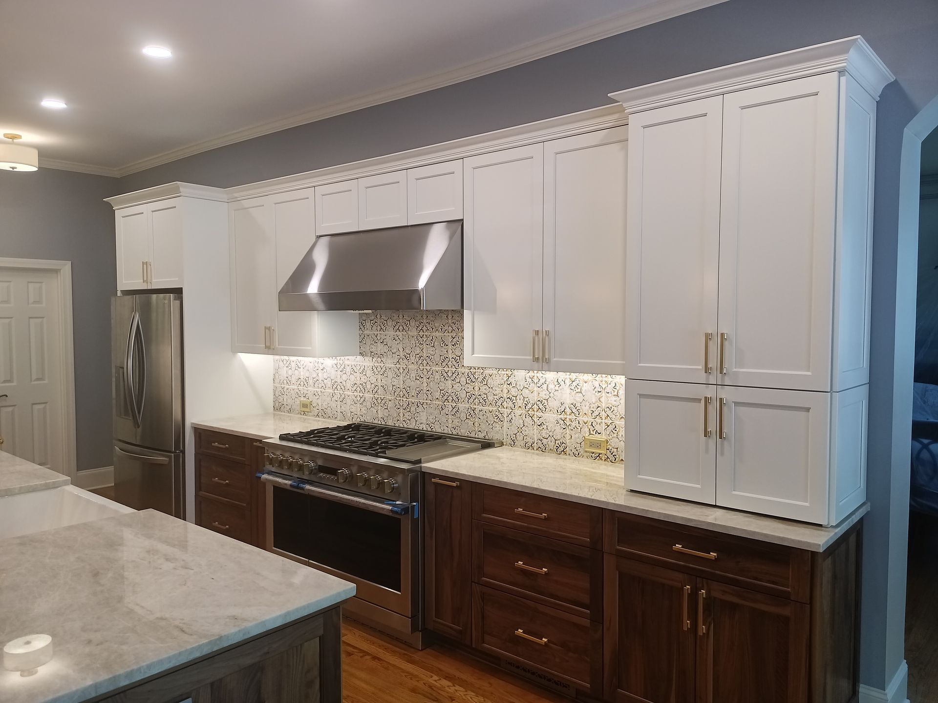 Kitchen with white upper cabinets, brown lower cabinets, stainless steel appliances, and a gray wall.