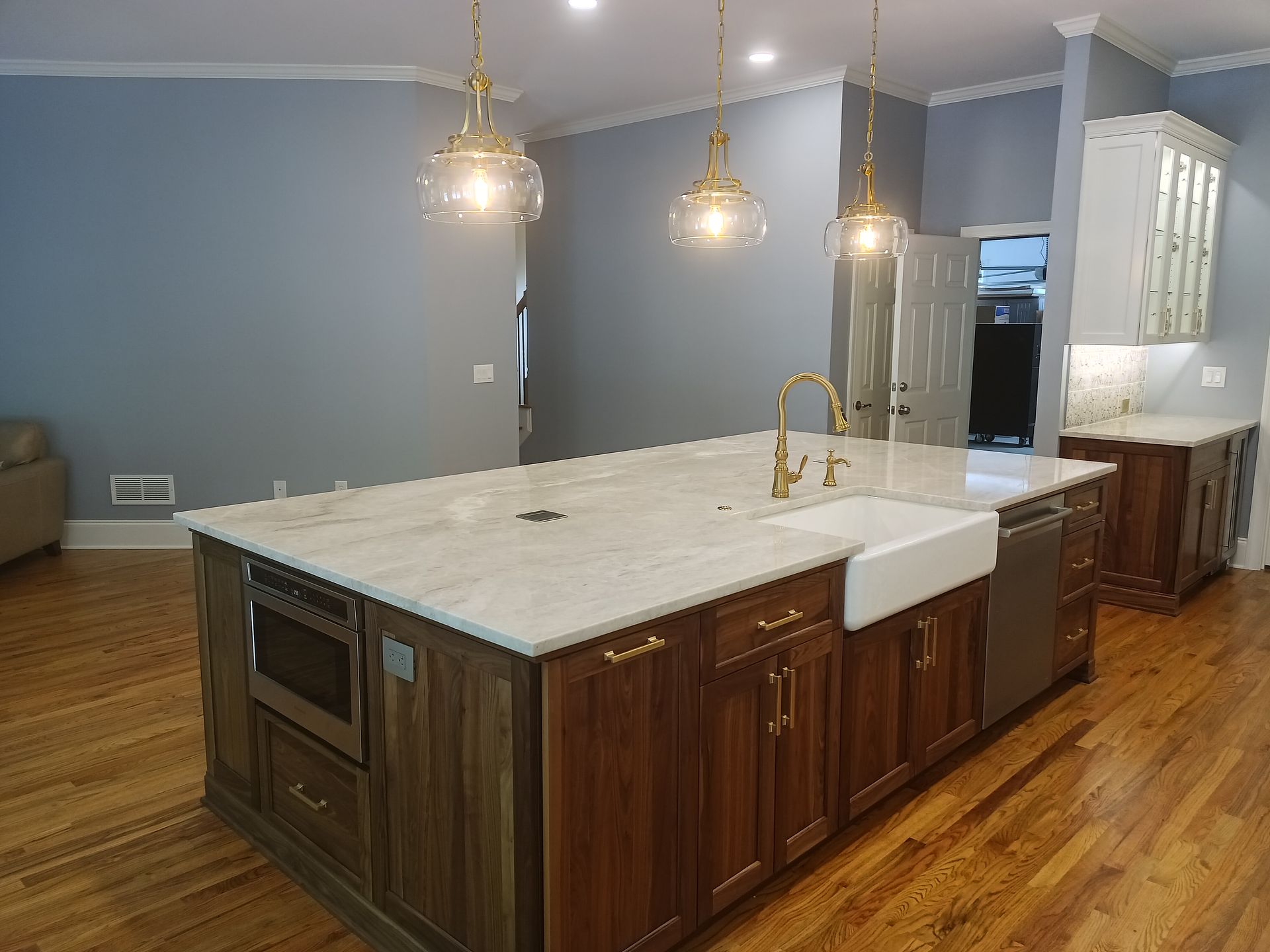 Kitchen island with wood cabinets, white countertop, sink, and gold fixtures, with pendant lights overhead.