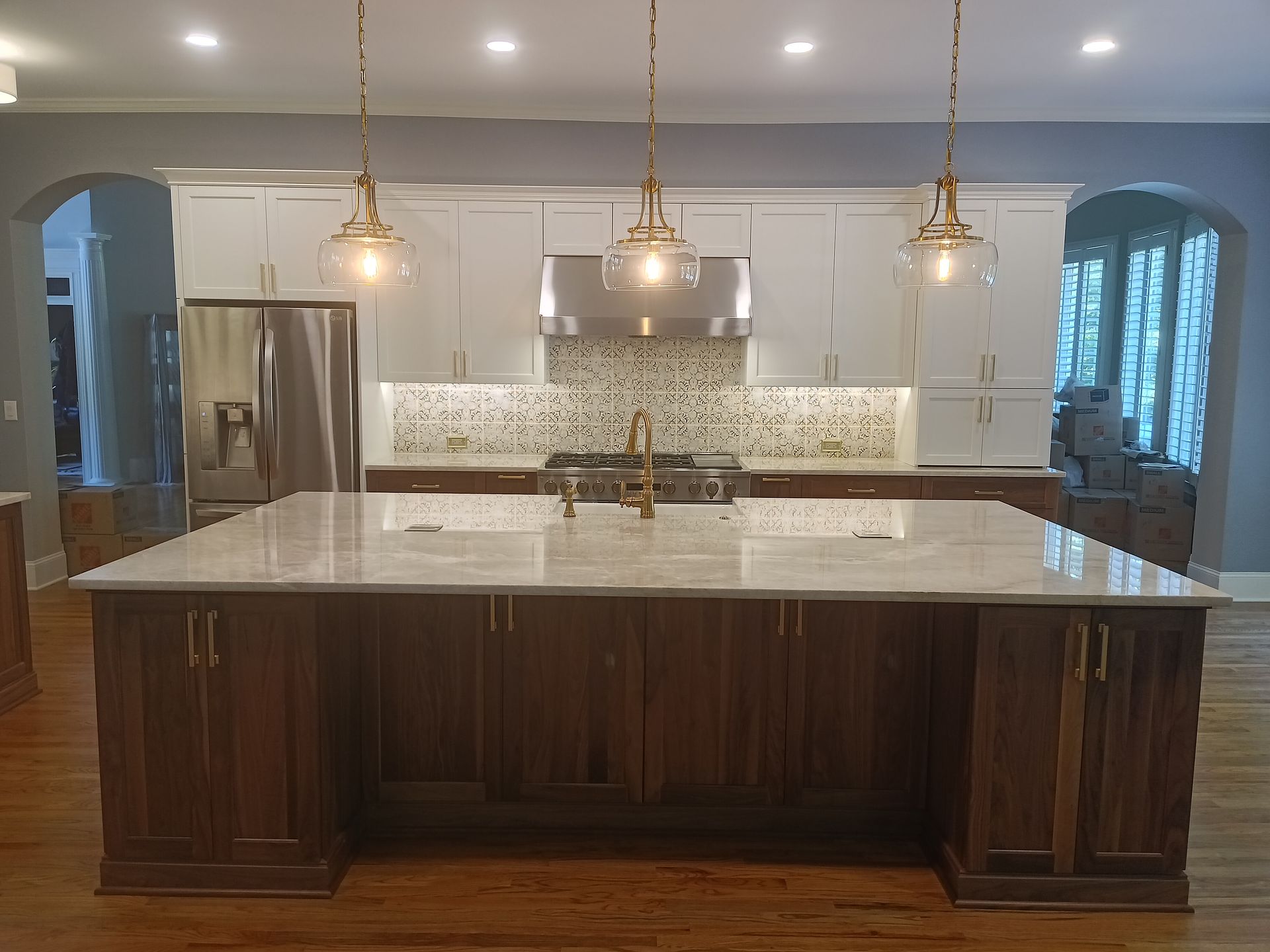 Modern kitchen with large island, white cabinets, gold light fixtures, and stainless steel appliances.