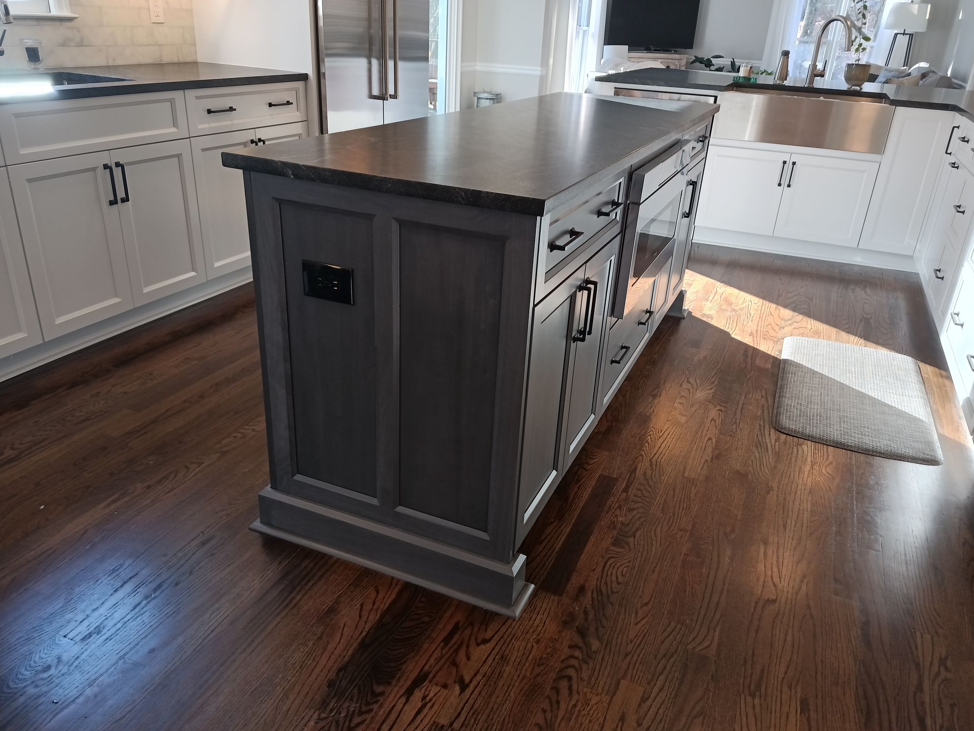 Gray kitchen island with dark countertop, hardwood floor, white cabinets in background.