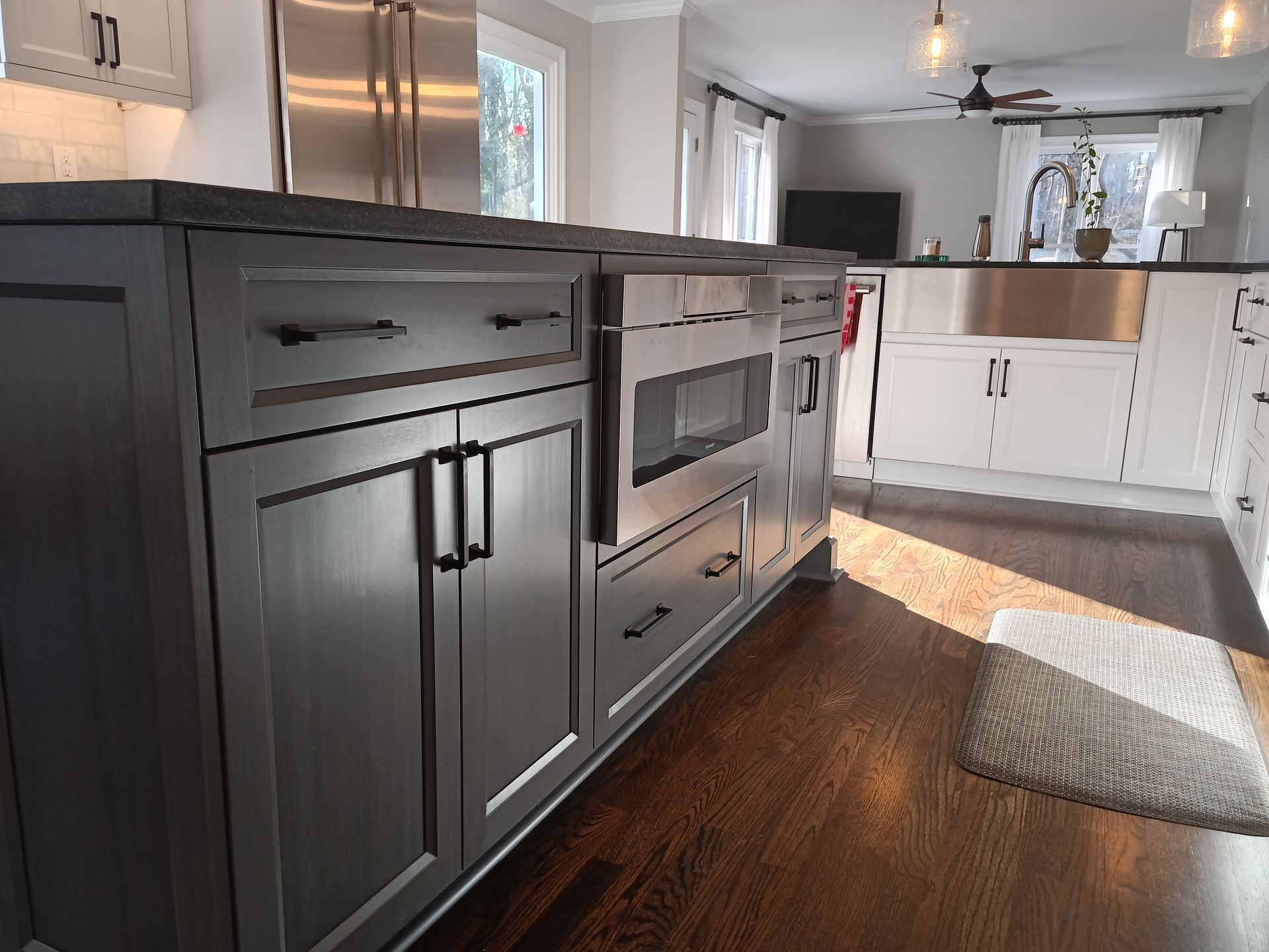 Gray kitchen island with built-in microwave and drawers; dark wood floors, white cabinets in the background.