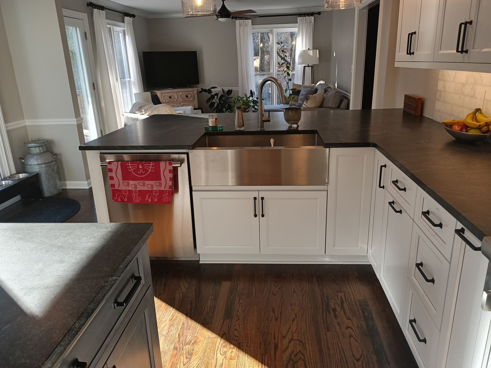 Kitchen with stainless steel sink, white cabinets, dark countertops, open to living room.