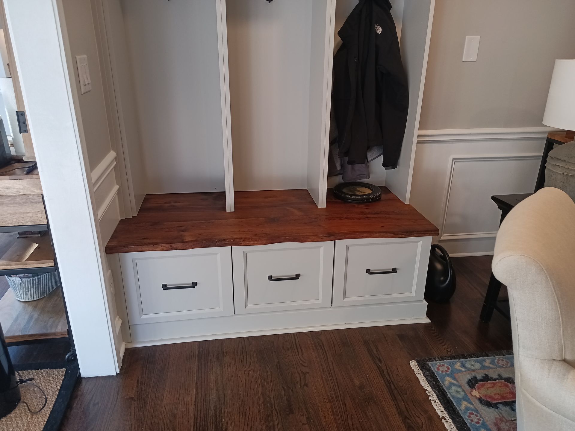 Built-in entryway storage with white drawers, a wooden bench, and coat hooks.