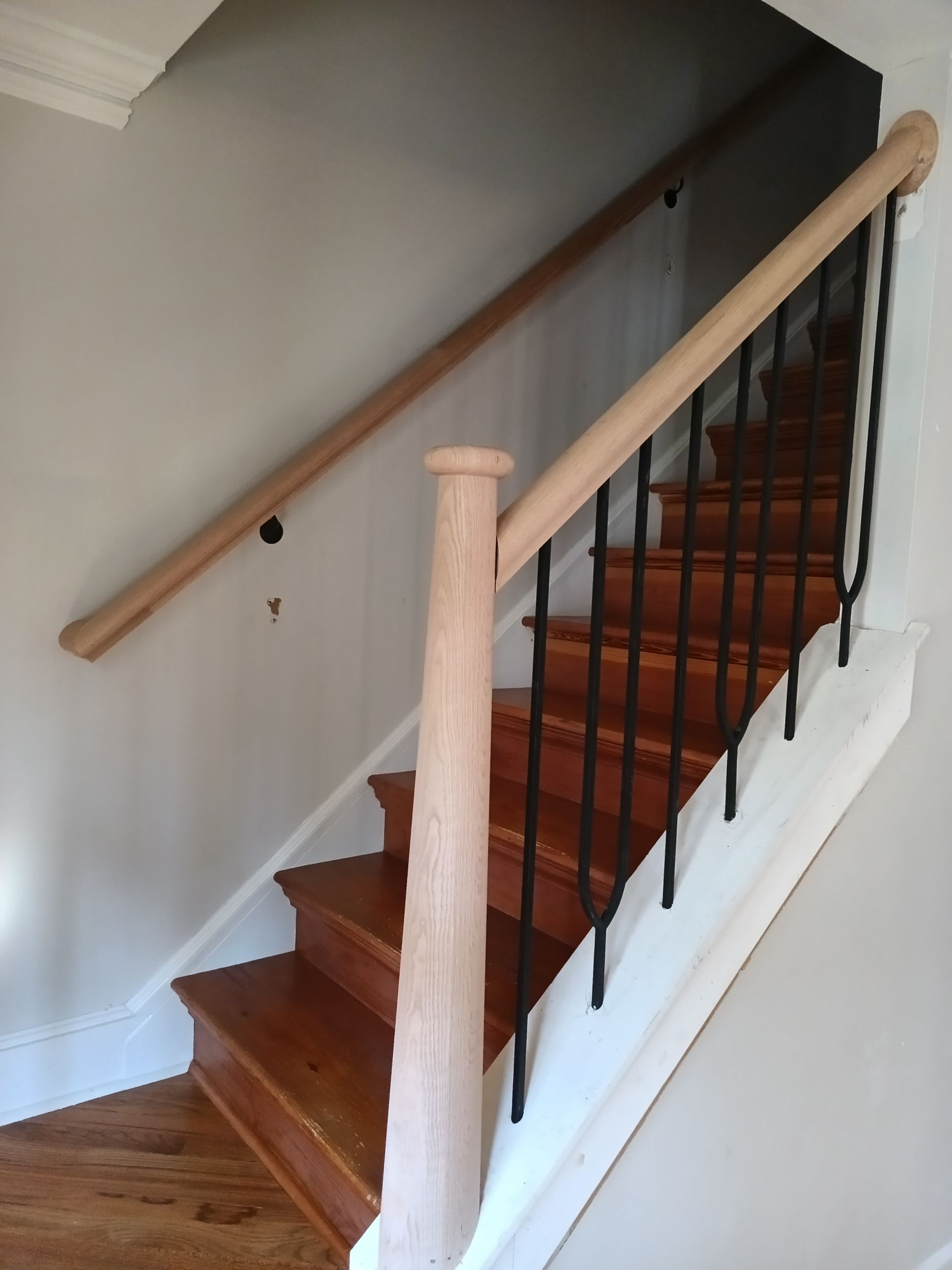 Wooden staircase with light wood handrails, black iron balusters, and white risers.