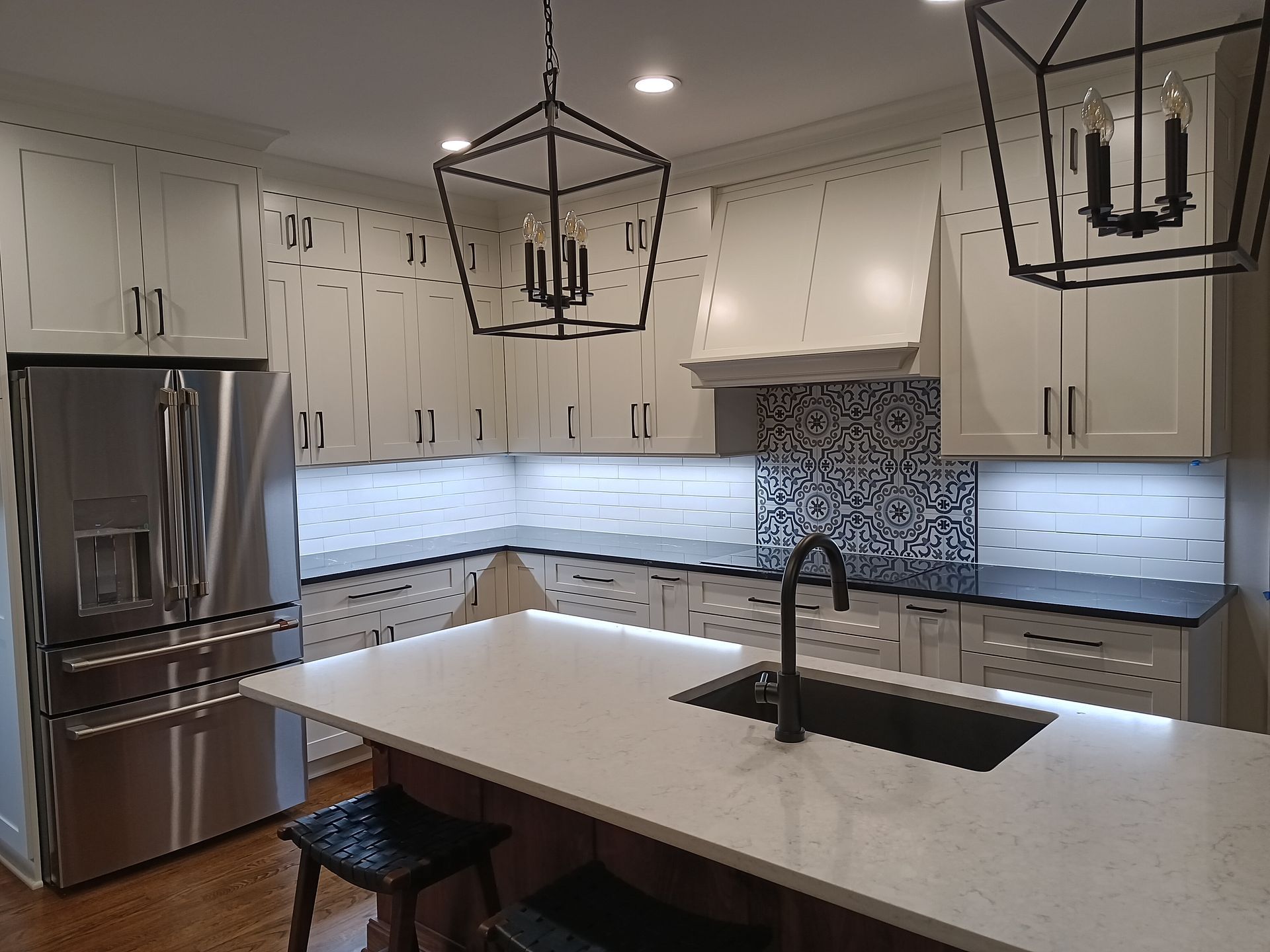 Modern kitchen with white cabinets, dark island, stainless steel fridge, and geometric tile backsplash.