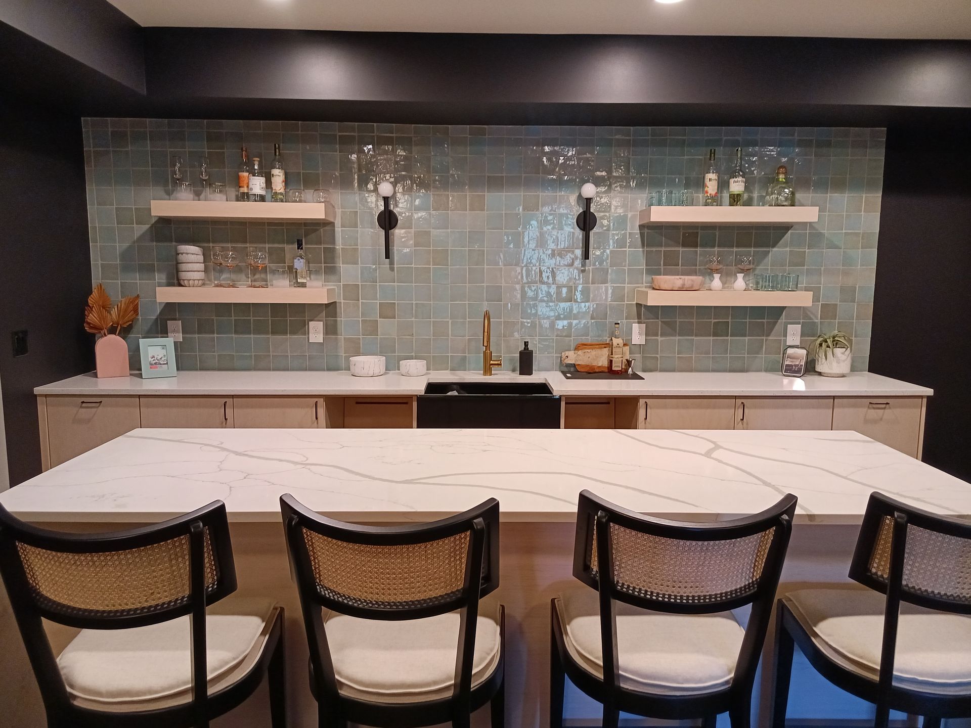 Bar area with white countertop and chairs, teal tile backsplash, floating shelves, and dark cabinetry.