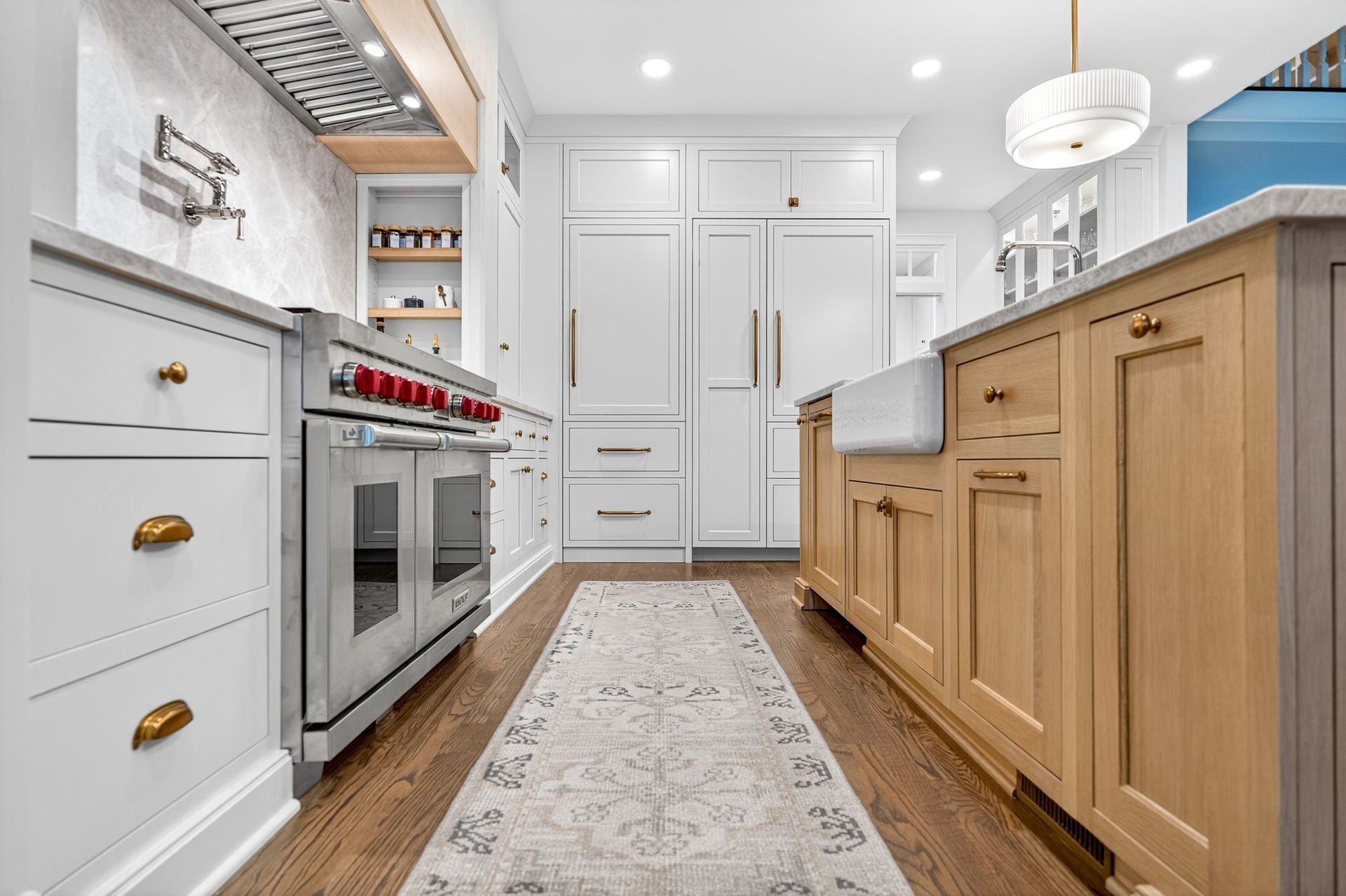 Stylish kitchen with white and natural wood cabinets, stainless steel appliances, and a patterned rug.