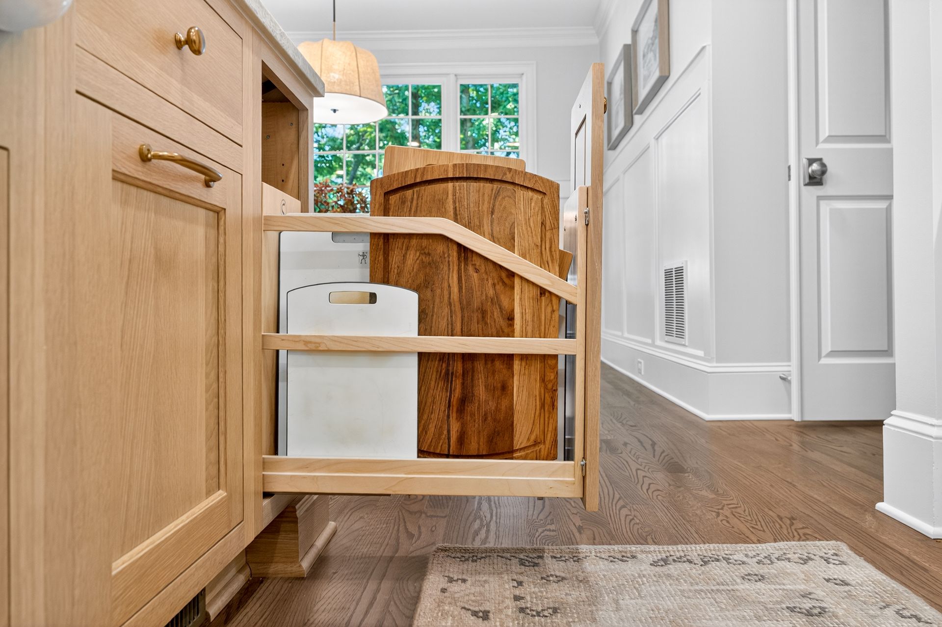 Pull-out cabinet with storage for a woven basket and white box in a light wood kitchen.