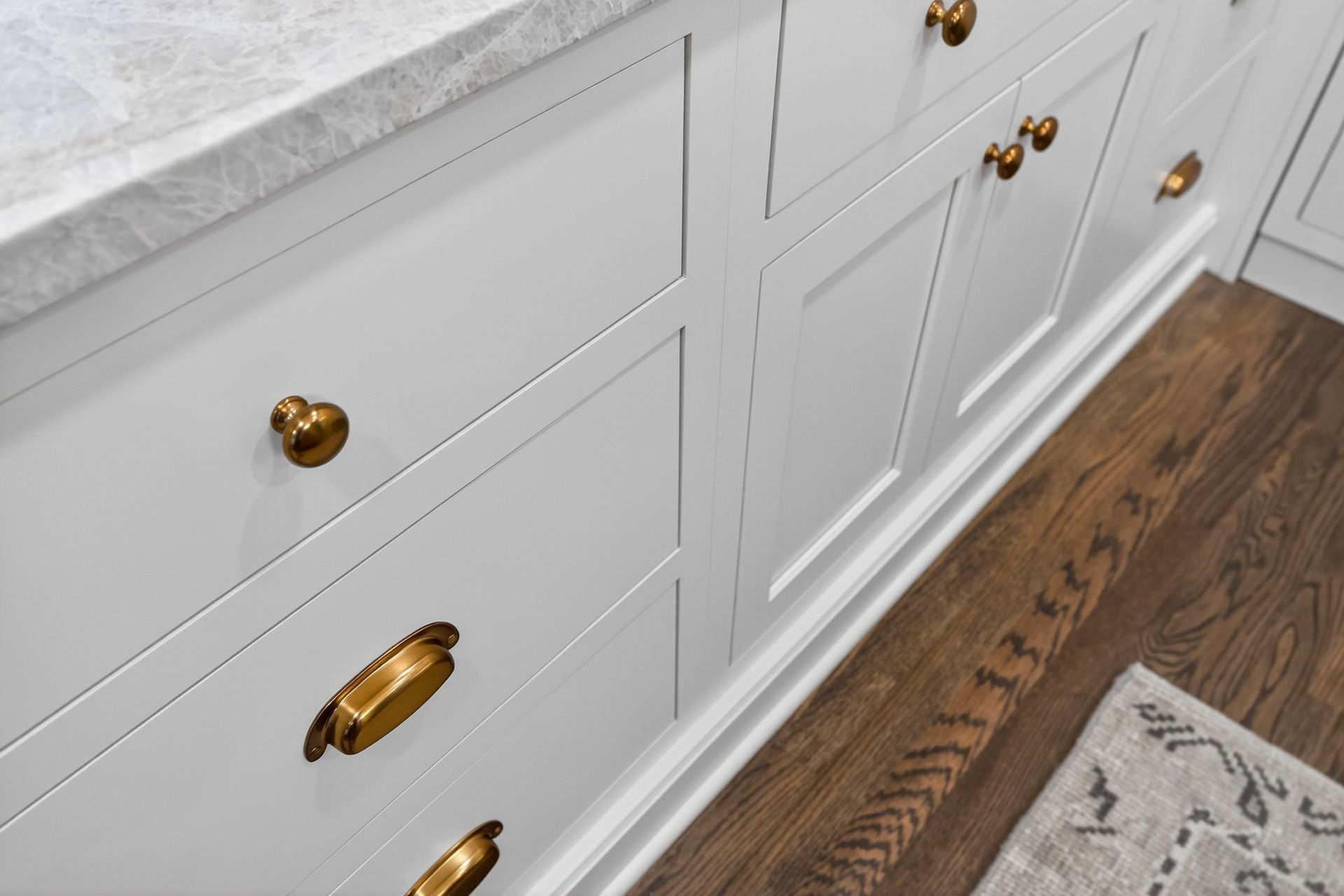 White kitchen cabinets with gold hardware and a marble countertop.